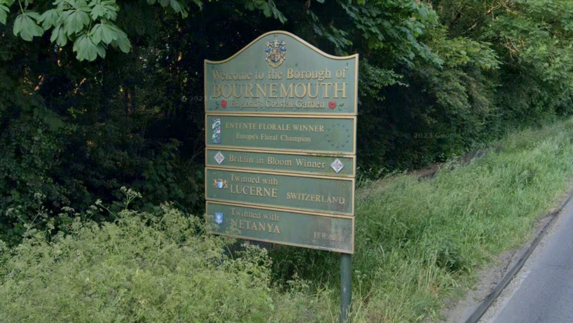 A welcome to Bournemouth sign next to the road. It is green and shows twinning arrangements between the town and others across the world. 