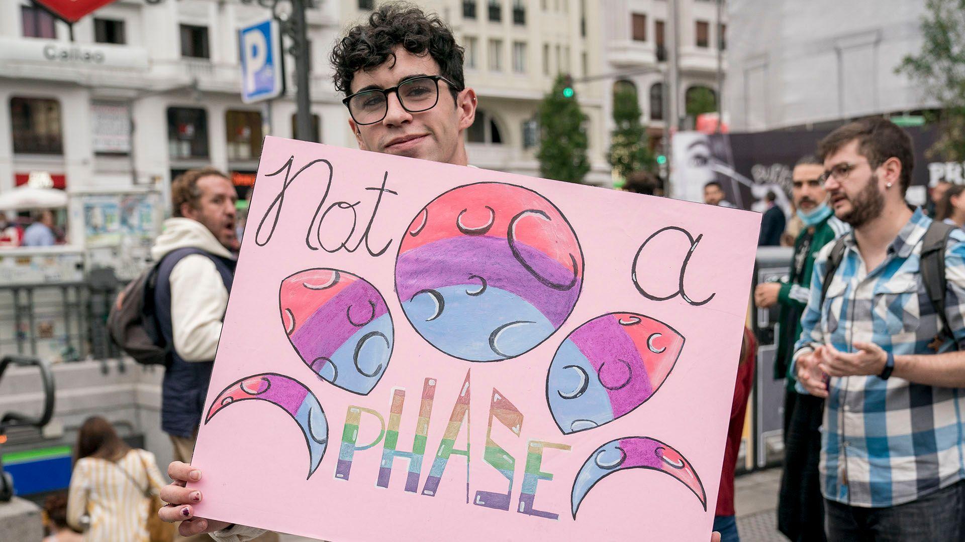 a man holding a sign featuring the bisexual flag and the words "not a phase"