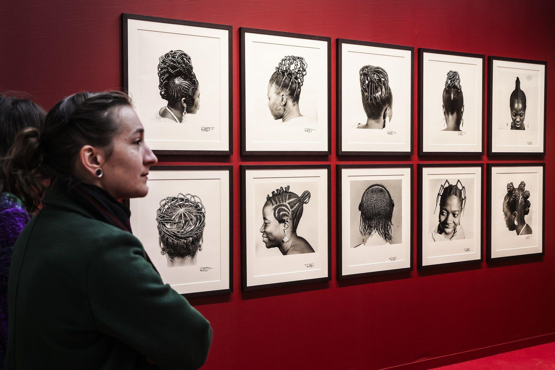 People walk past 10 framed photographs of different braided hairstyles hung on a wall painted maroon during the Paris Photo fair at the Grand Palais in Paris, France -  Wednesday 6 November 2024