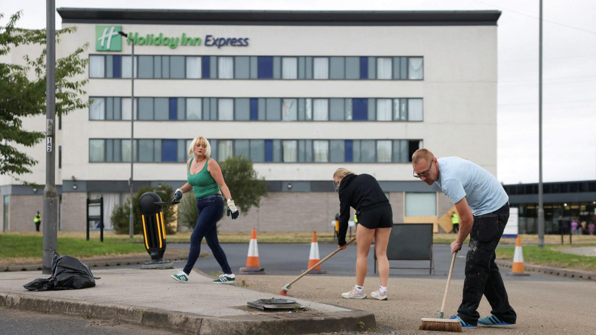 Three people are pictured outside the hotel. Two are holding brooms and seem to be cleaning the ground.
