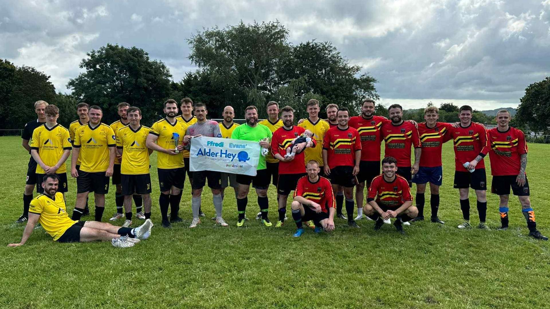 Llun yn dilyn gem elusennol rhwng ffrindiau Arron a chwaraewyr y Gogledd yn dal baner Alder Hey
