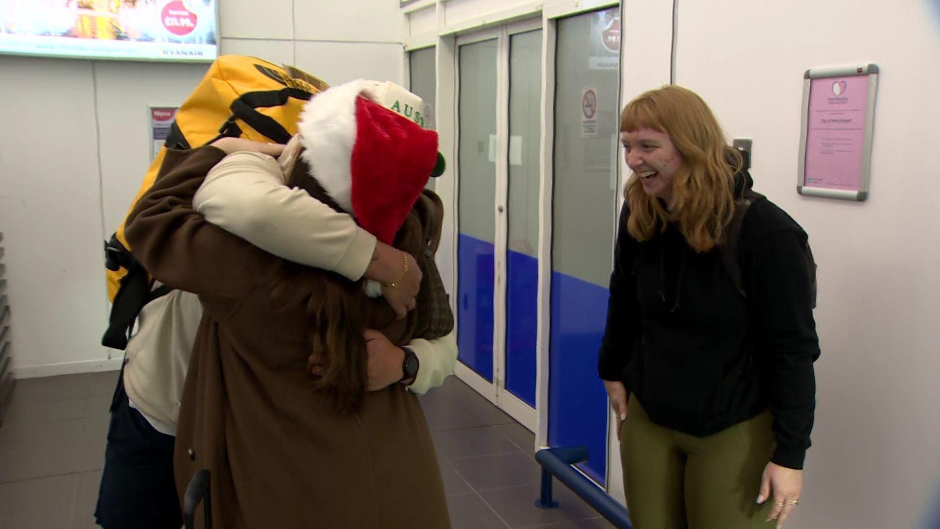 Kate is on the right, with ginger hair and a fringe. She is wearing a black hoodie and green leggings. Aoife and Zhenhua are hugging and wearing Santa hats.