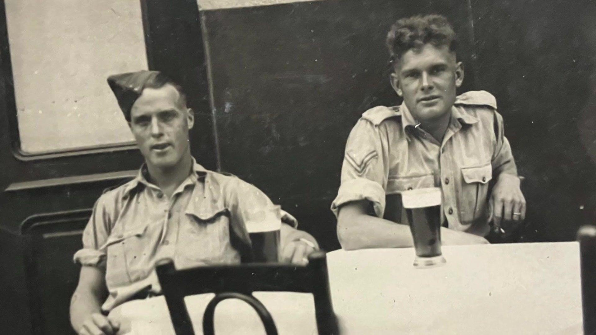 A black and white photo showing Fred and Percy sat in uniform at a table in a café with drinks on a table in front of them.