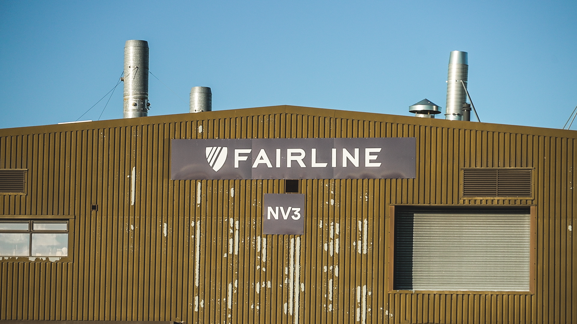 A yellow corrugated metal building with a "Fairline" logo on a black banner.