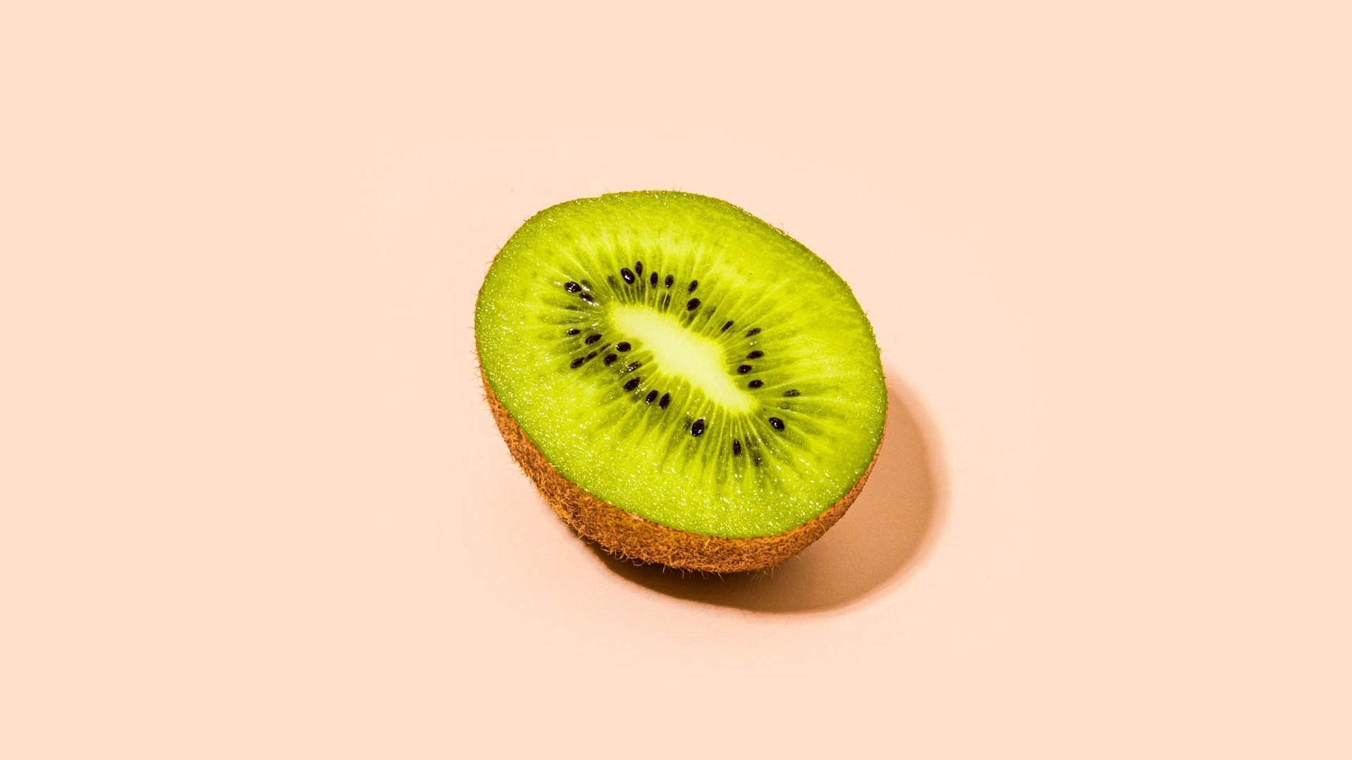 half a kiwi sliced length ways on a pale orange background