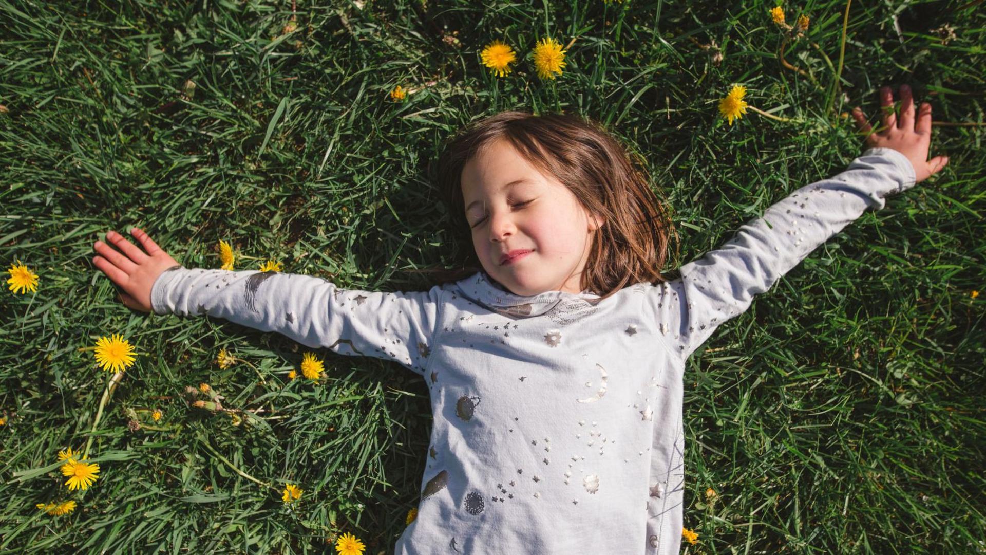 little girl enjoying sunshine lying down in grass with flowers