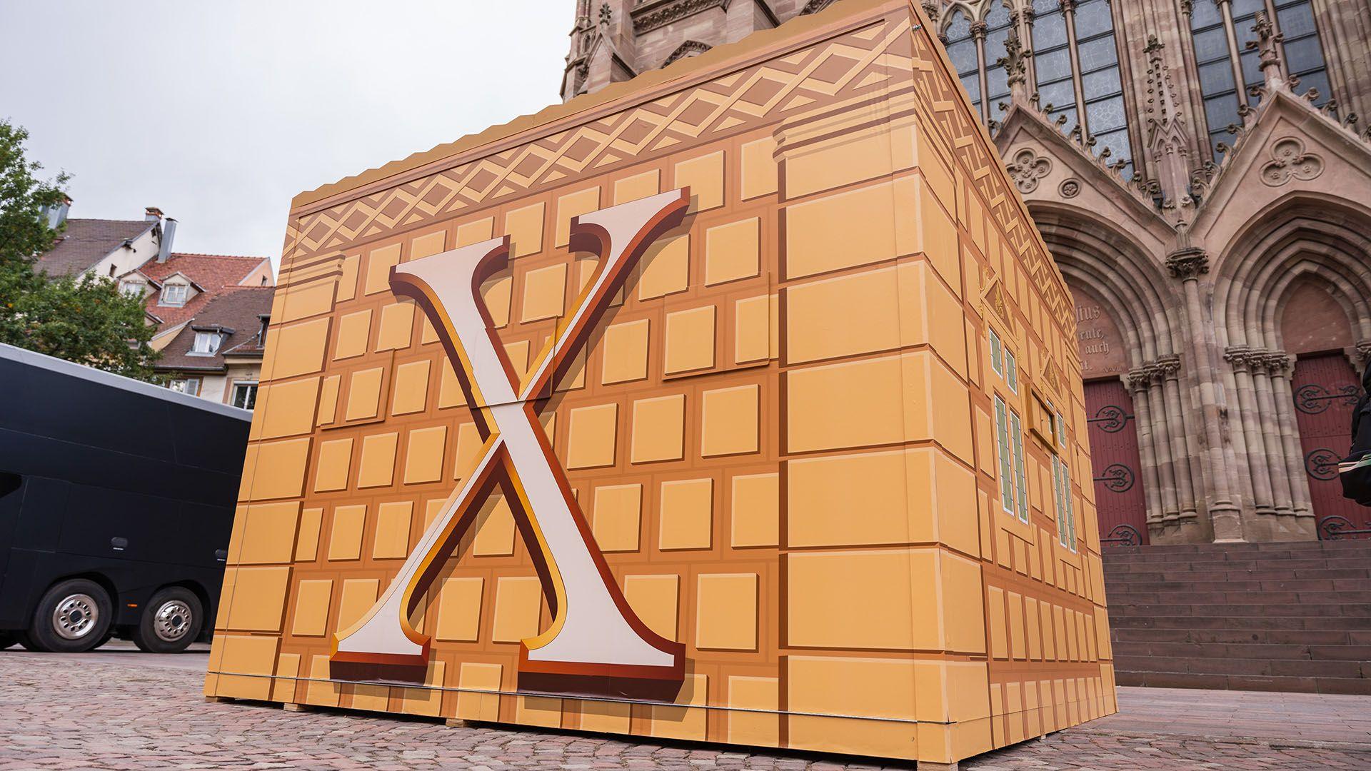 a large box with an x on its side stands in front of a cathedral