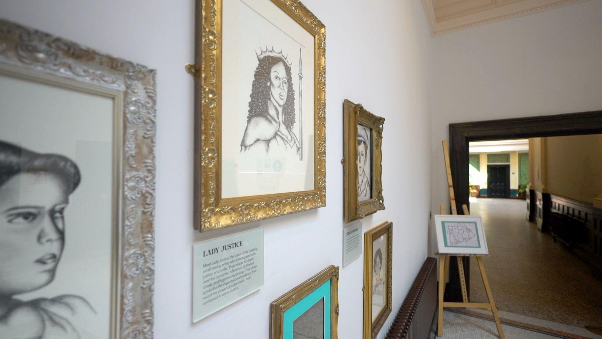 A white wall with pencil portraits hanging up in golden frames