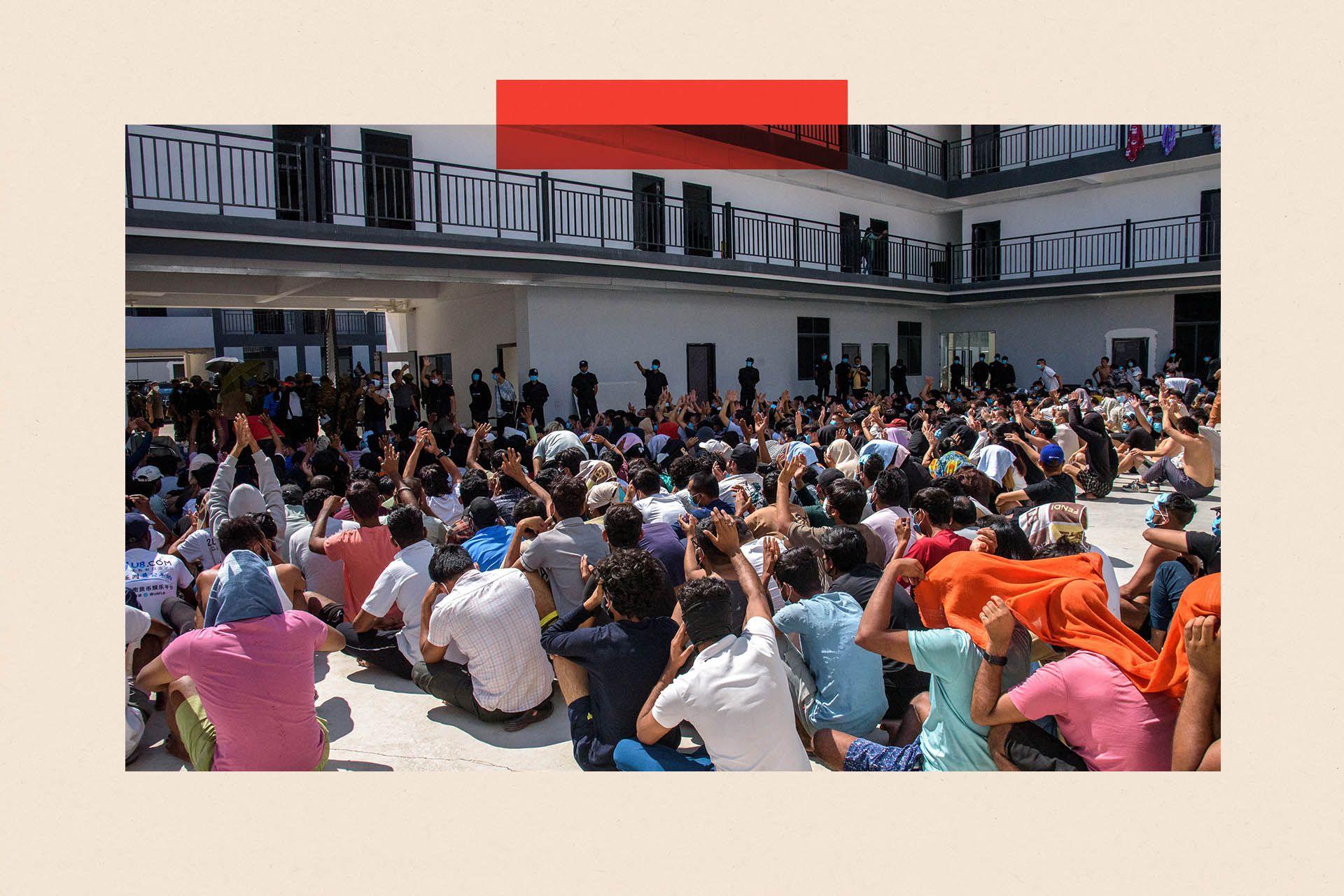 Hundreds of people sit cross legged in rows on a floor in an outdoors atrium