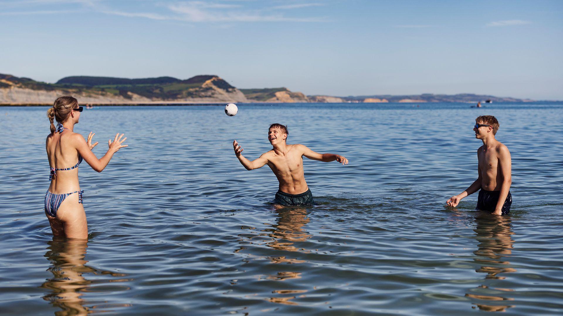 Teenagers enjoying the seaside in Dorset, United Kingdom. They are playing with a small  ball while standing in the sea.