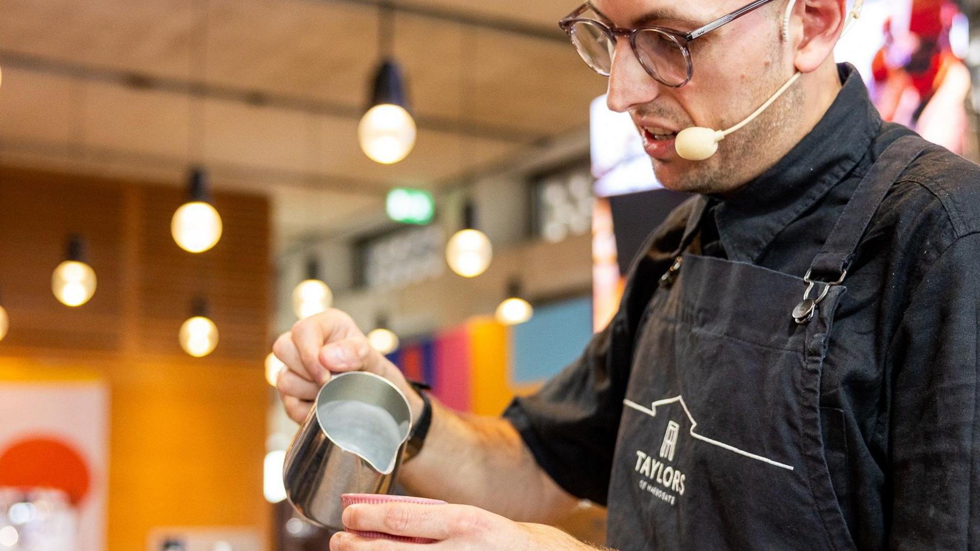Will Woodhouse-Banks pours milk from a metal jug into a cup