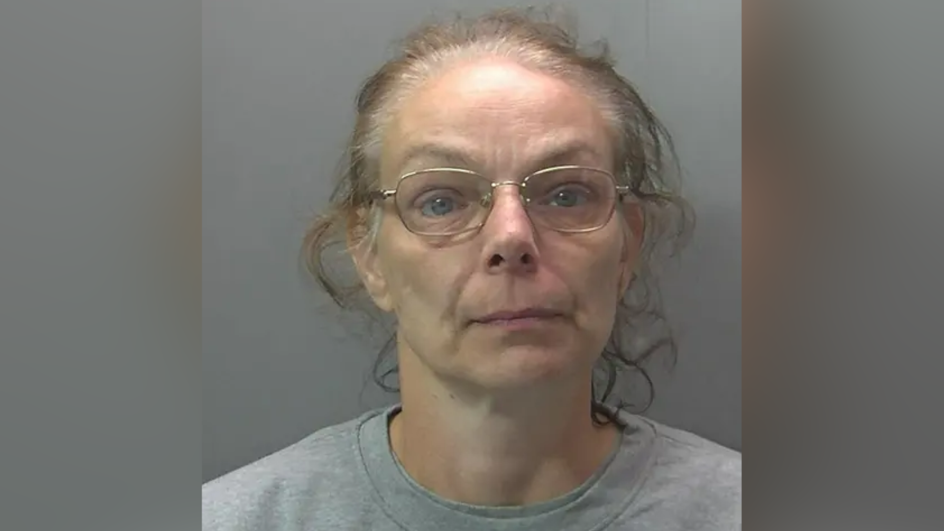 Custody photo of Melanie Wright. She has curly greying hair that has been tied back from her face and is wearing thin framed gold rimmed glasses. She is also wearing a plain grey sweatshirt.