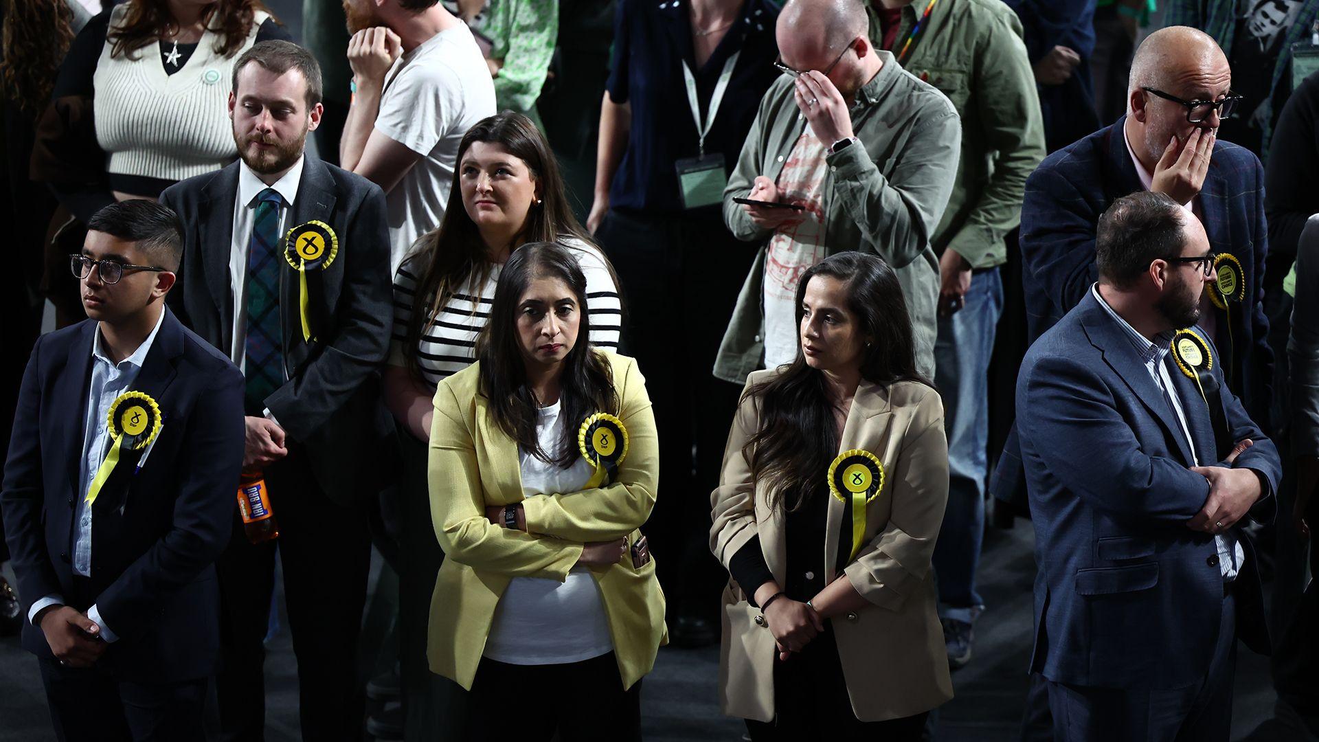 Supporters of the SNP, wearing yellow rosettes, looking sad and disappointed 