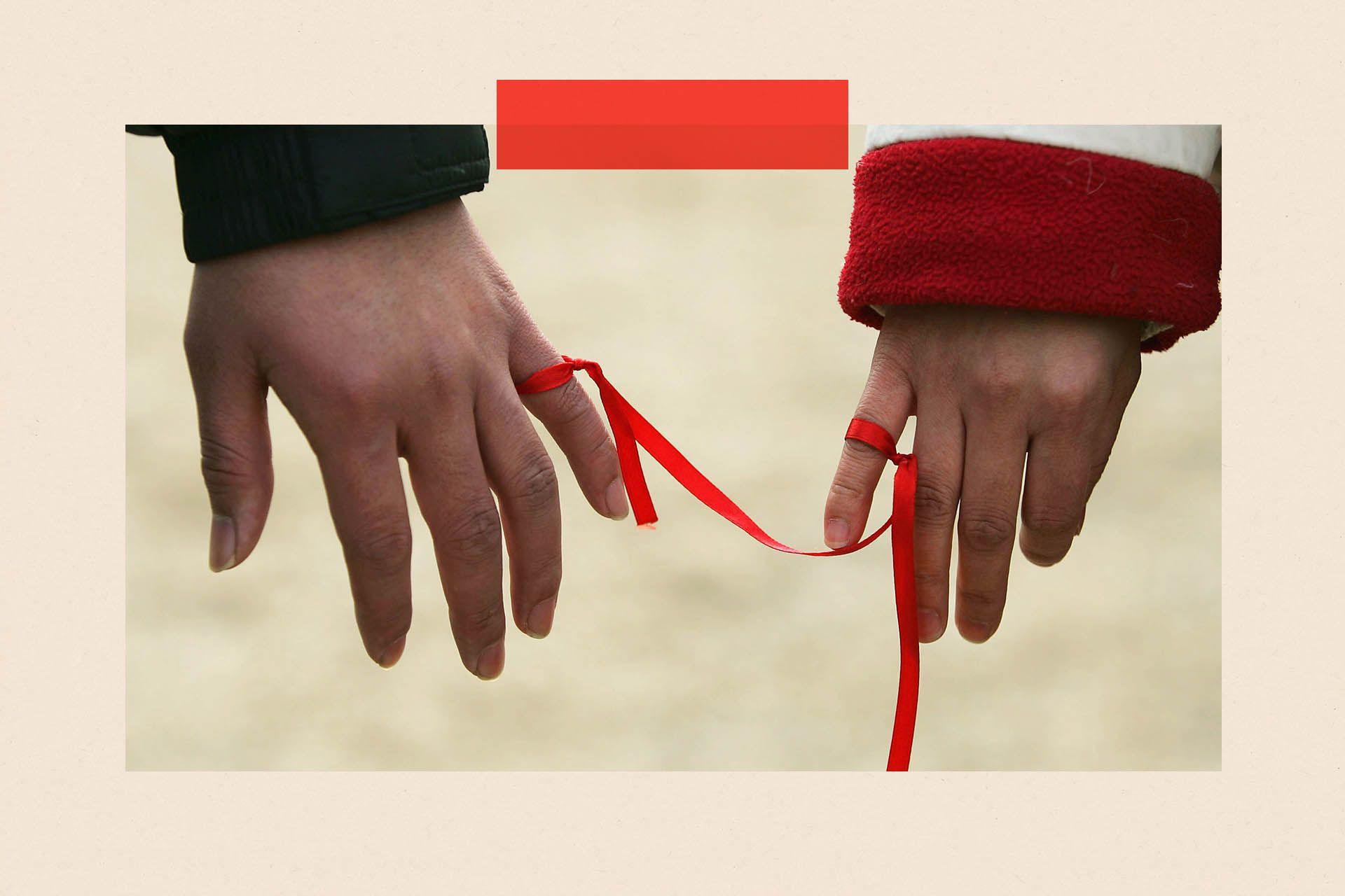 Two people tie a red ribbon to their little fingers