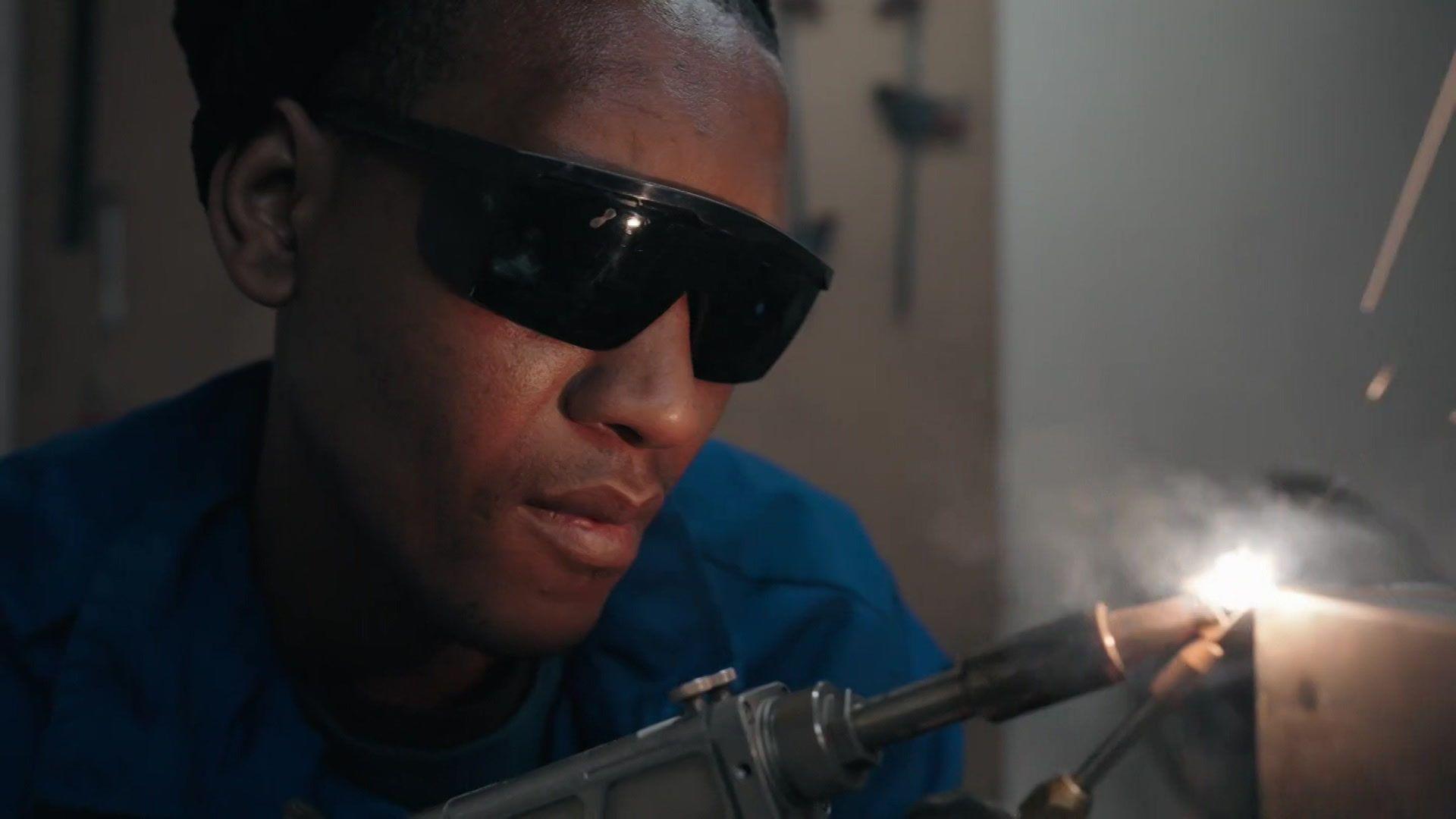 A close-up of a welder wearing dark glasses and welding some metal.