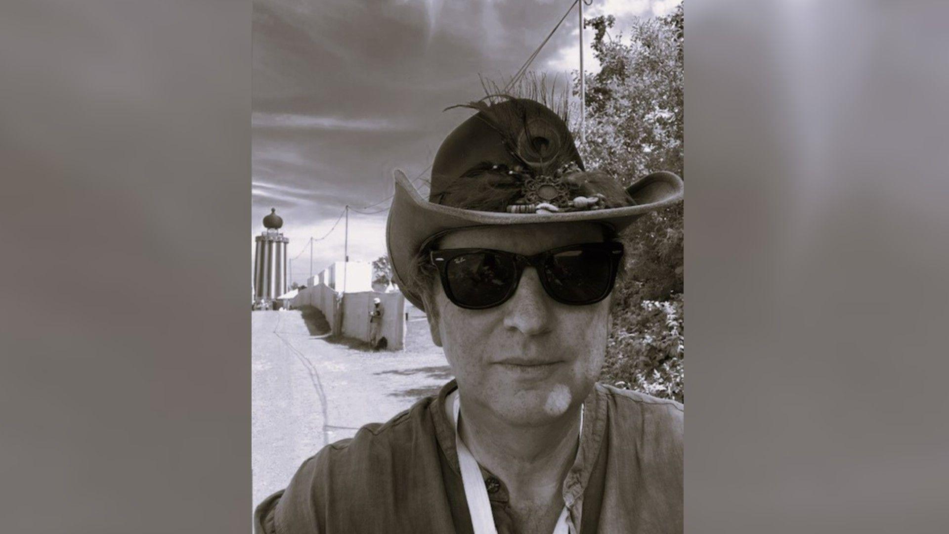 A black and white photograph of a man wearing sunglasses and a cowboy hat