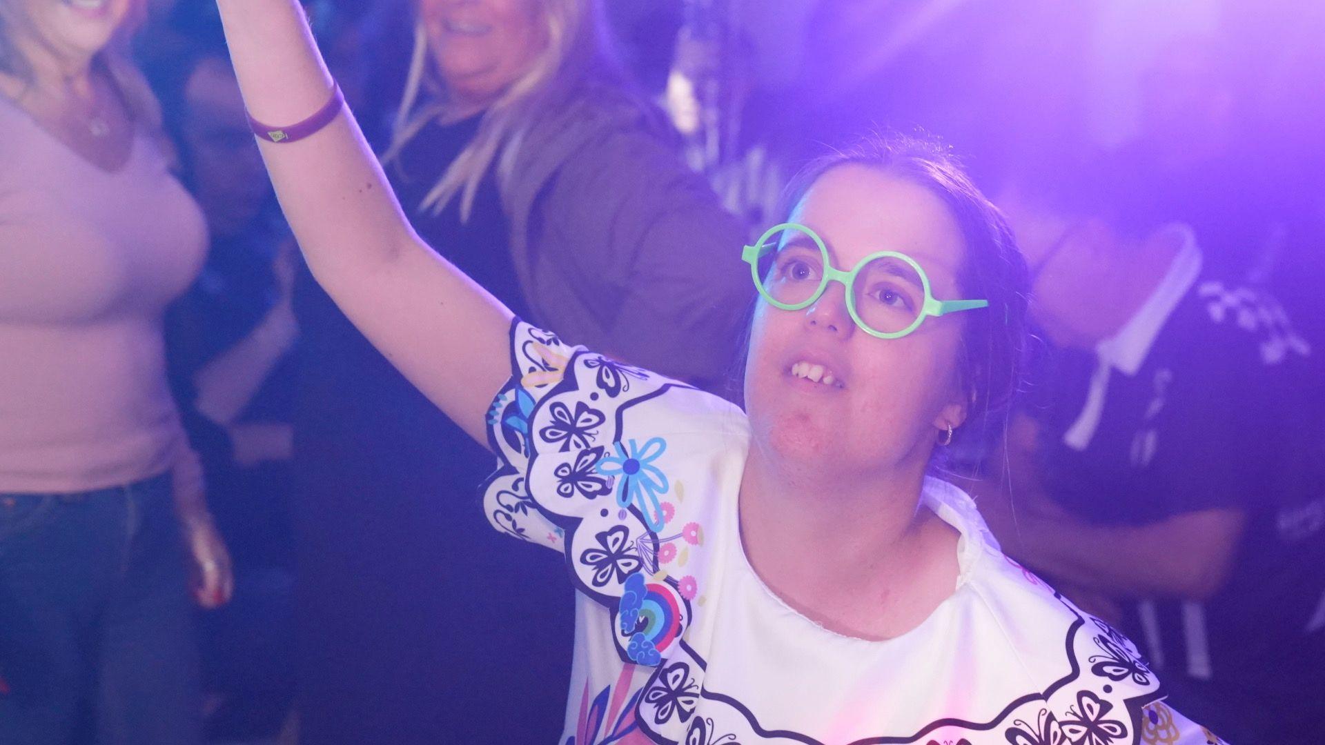 A woman in an Encanto themed outfit and green glasses dancing on the dance floor.