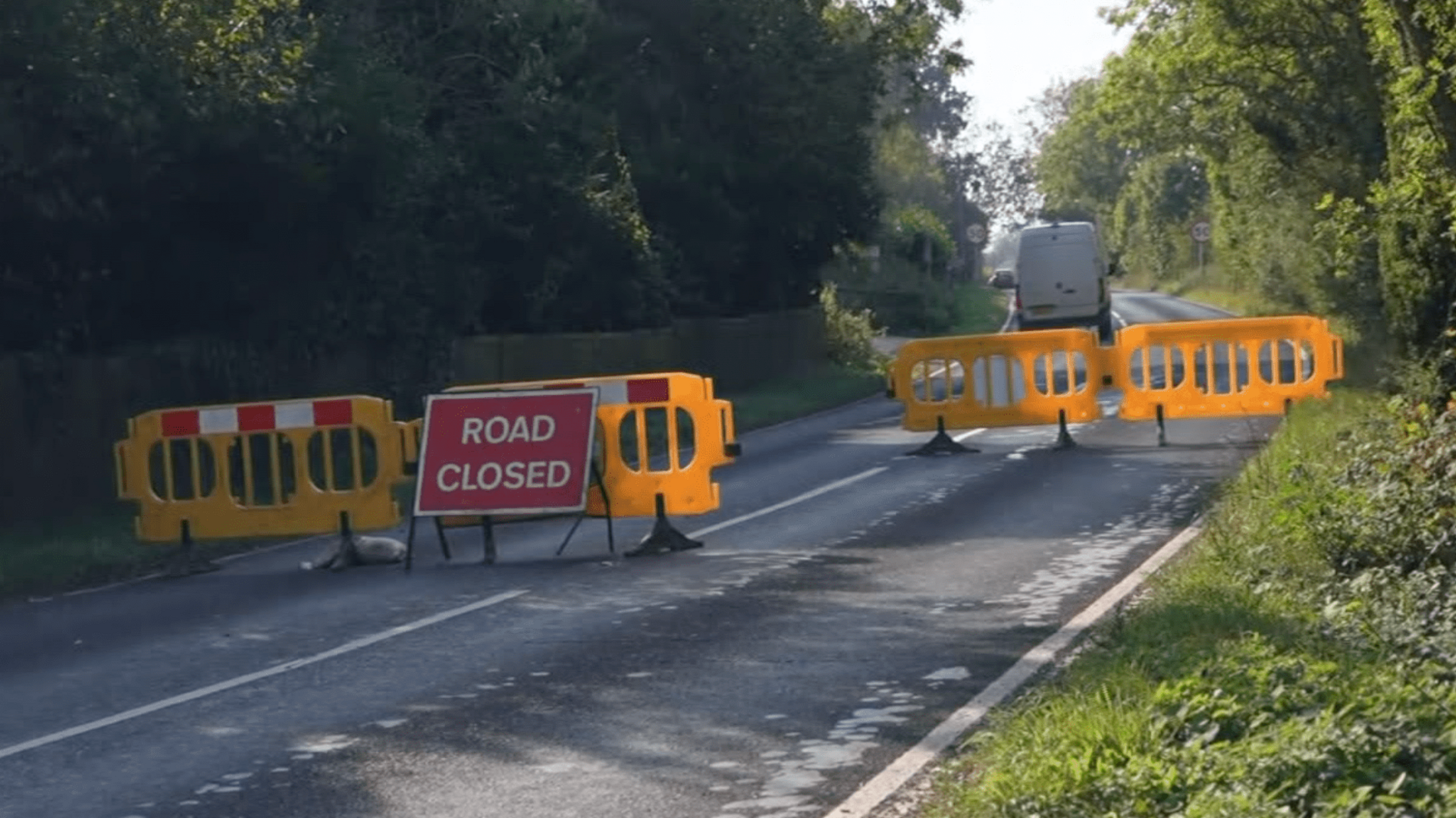 A rural road with yellow plastic barriers and one red sign, reading "road closed". 