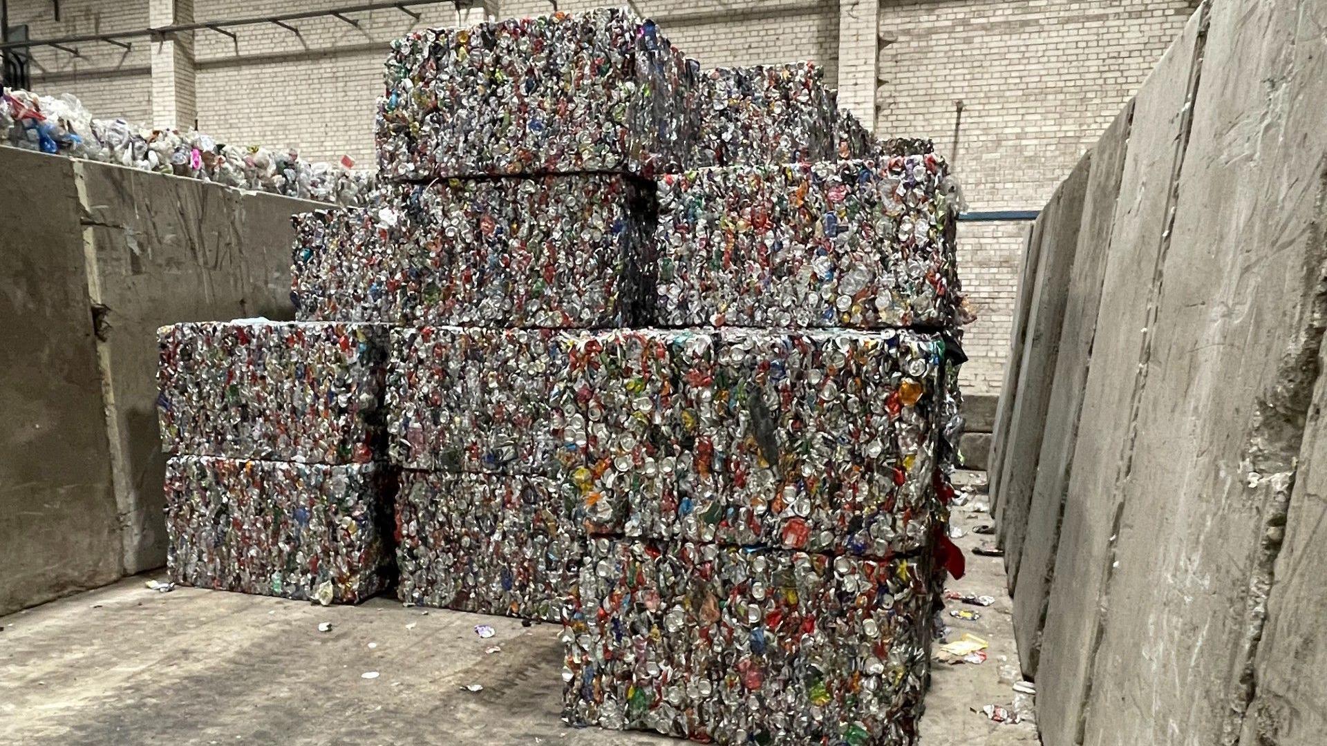 Bales of crushed recycling are piled on top of each other inside a recycling centre.