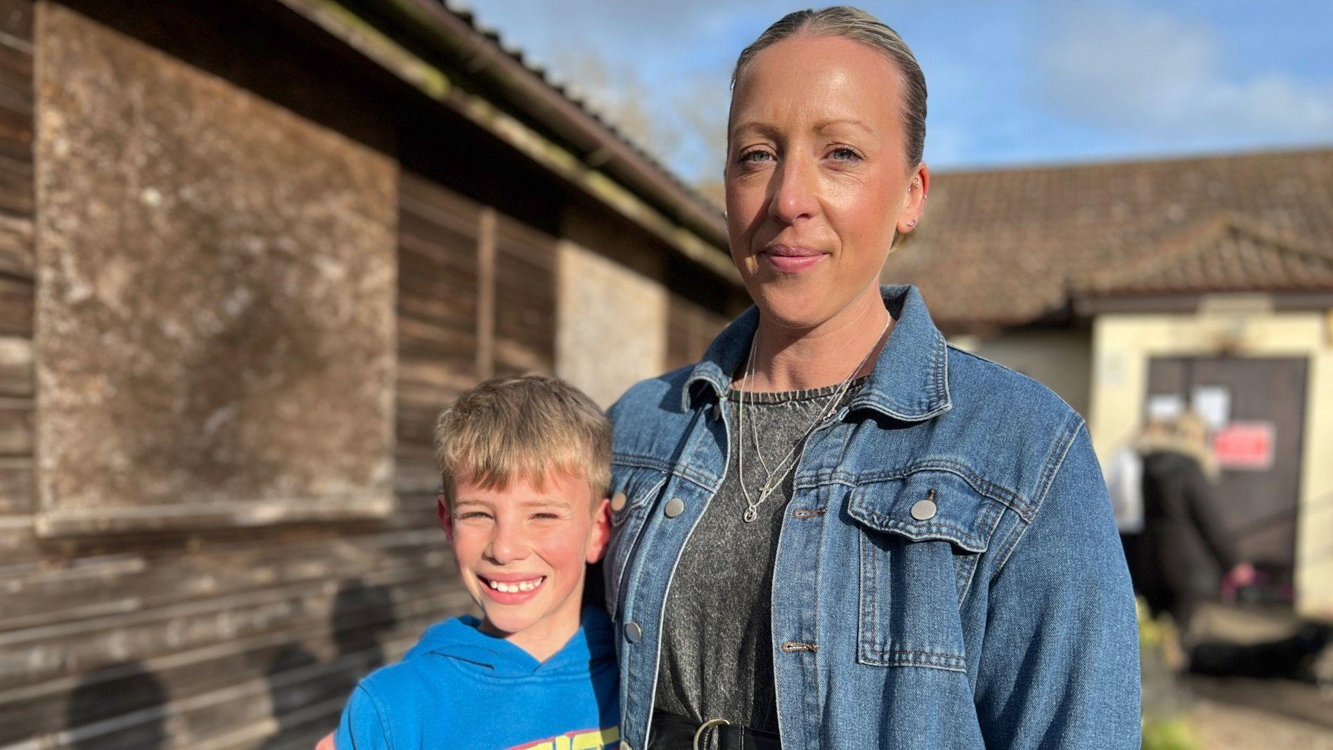 Marie Snell, wearing a denim jacket and grey top stands next to her son Dexter - he wears a royal blue hoodie and is smiling at the camera