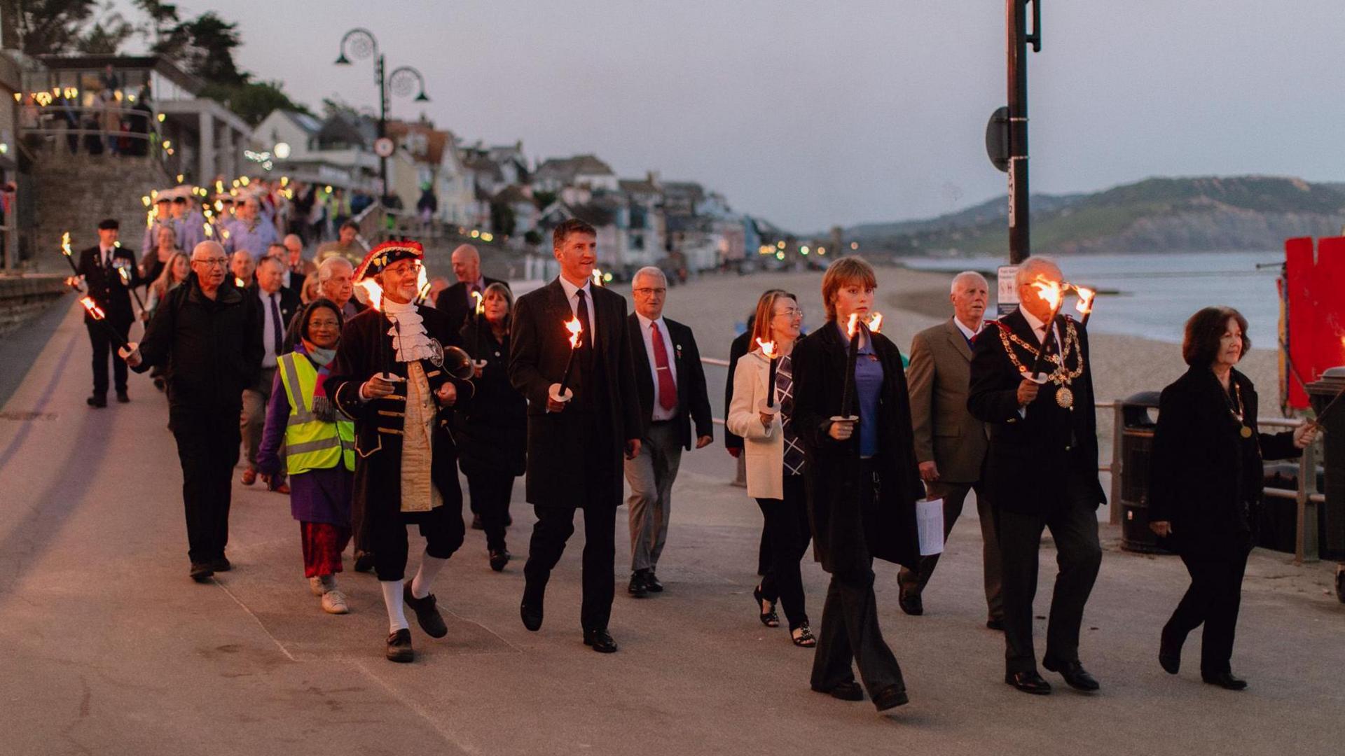 A procession of about 100 people carrying torches on the promenade at Lyme Regis