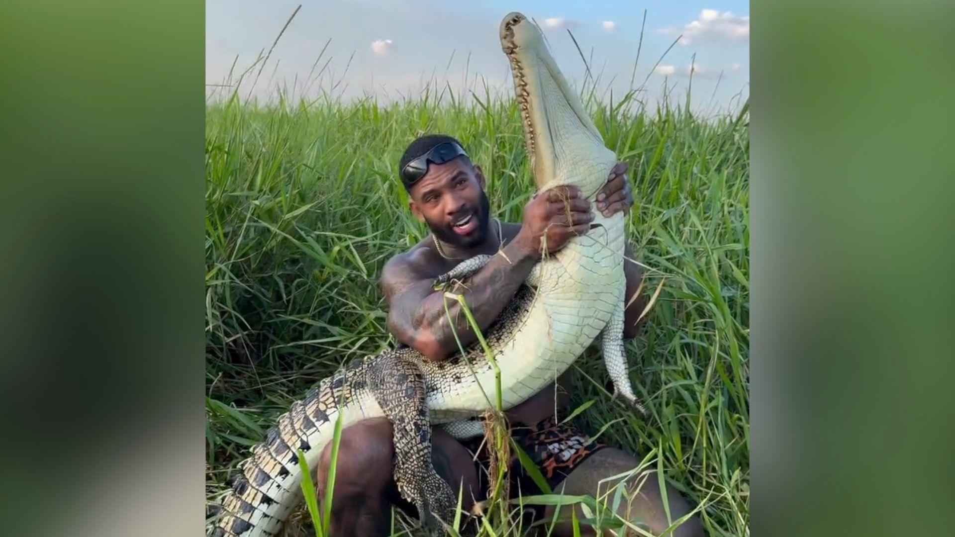 Mike Holston is seen holding a juvenile saltwater croc around the neck in grassland