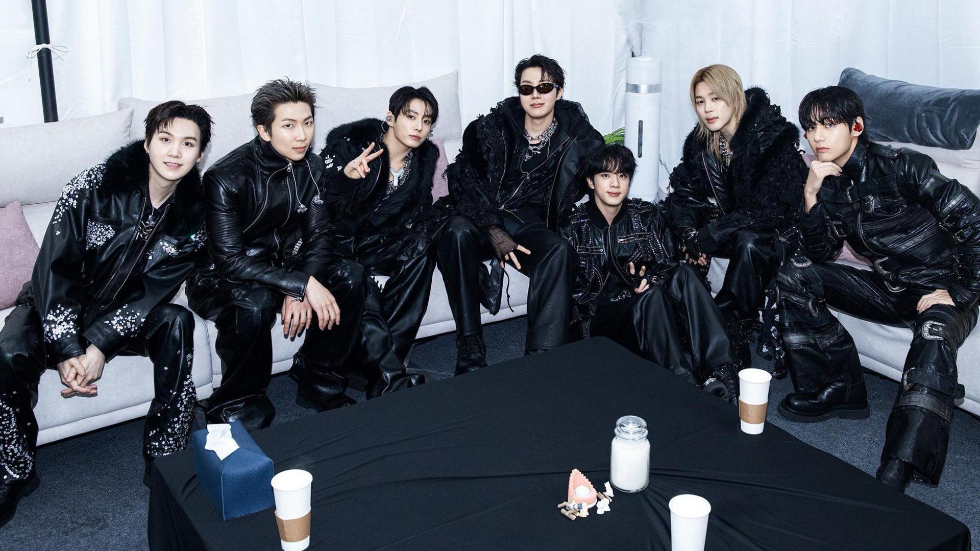 The seven BTS members, dressed in black from top to toe, sitting around a couch before their show in Goyang, South Korea