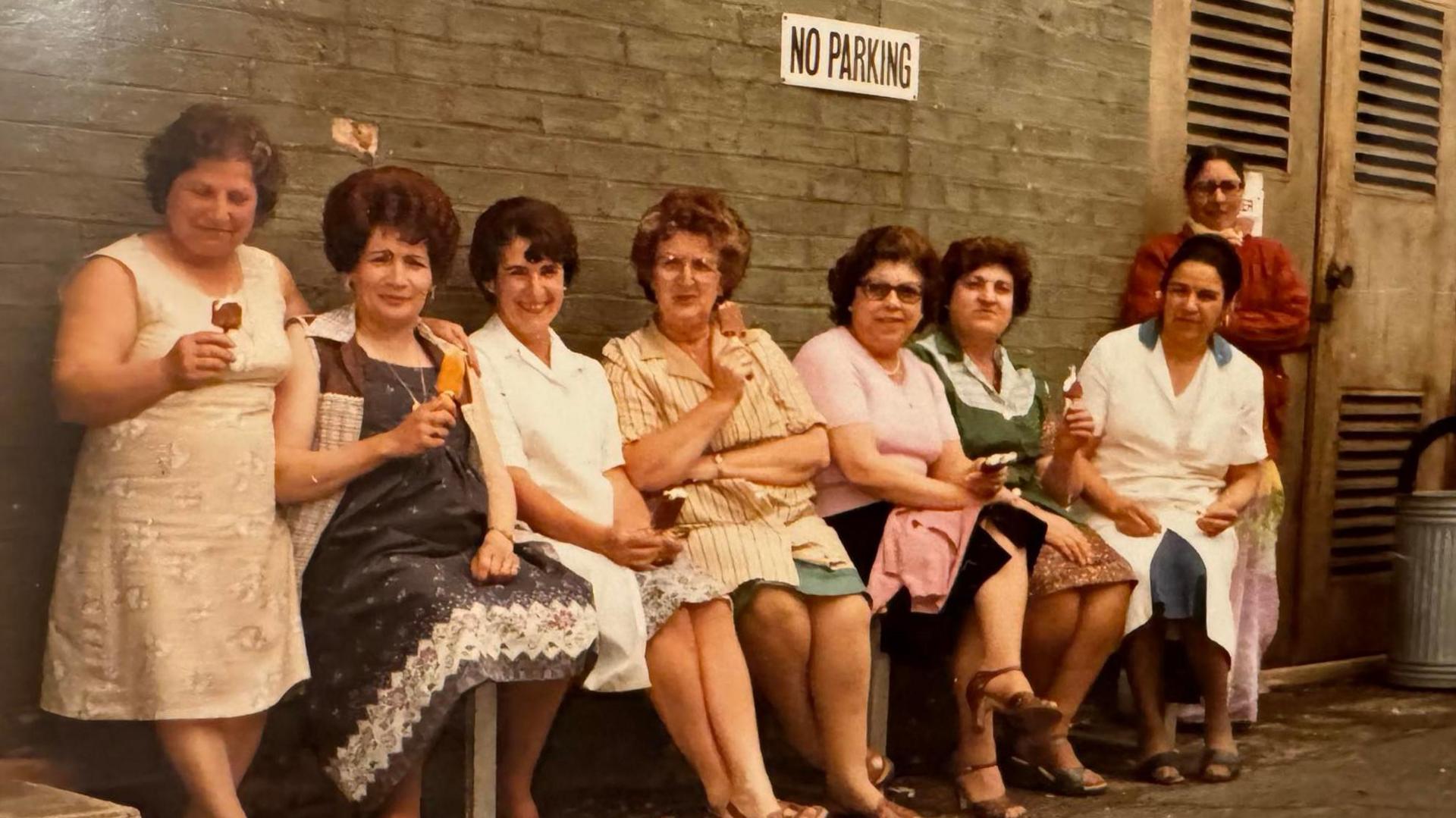 A group of women eating ice creams sitting on a bench in the 1970s.