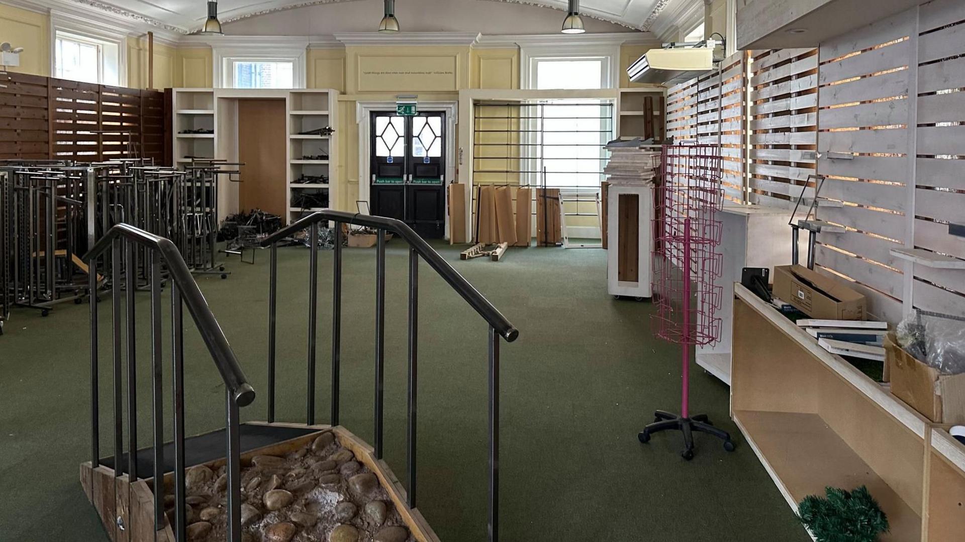 An empty shop with shelves along the walls, in the middle of the image is a walkway with rocks embedded on it to test walking shoes.
