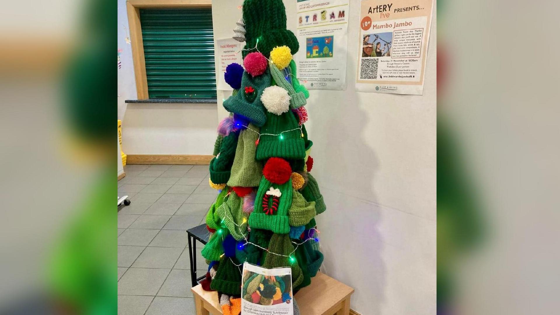 The tree sits on a table with lights around the hats - the bobbles are knitted in different colours to imitate baubles.