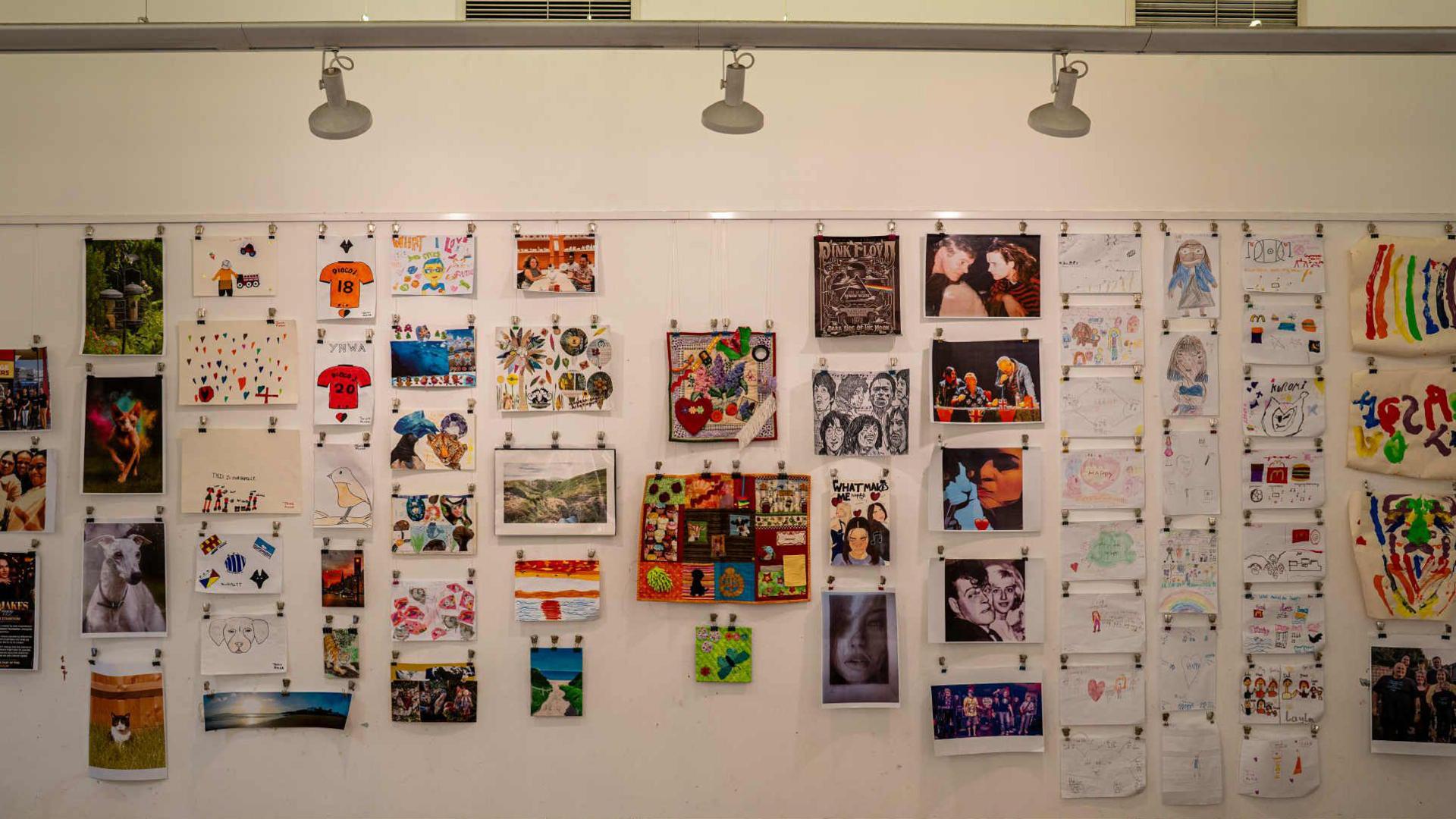 Drawings, photos and paintings displayed on a white gallery wall in a grid formation.