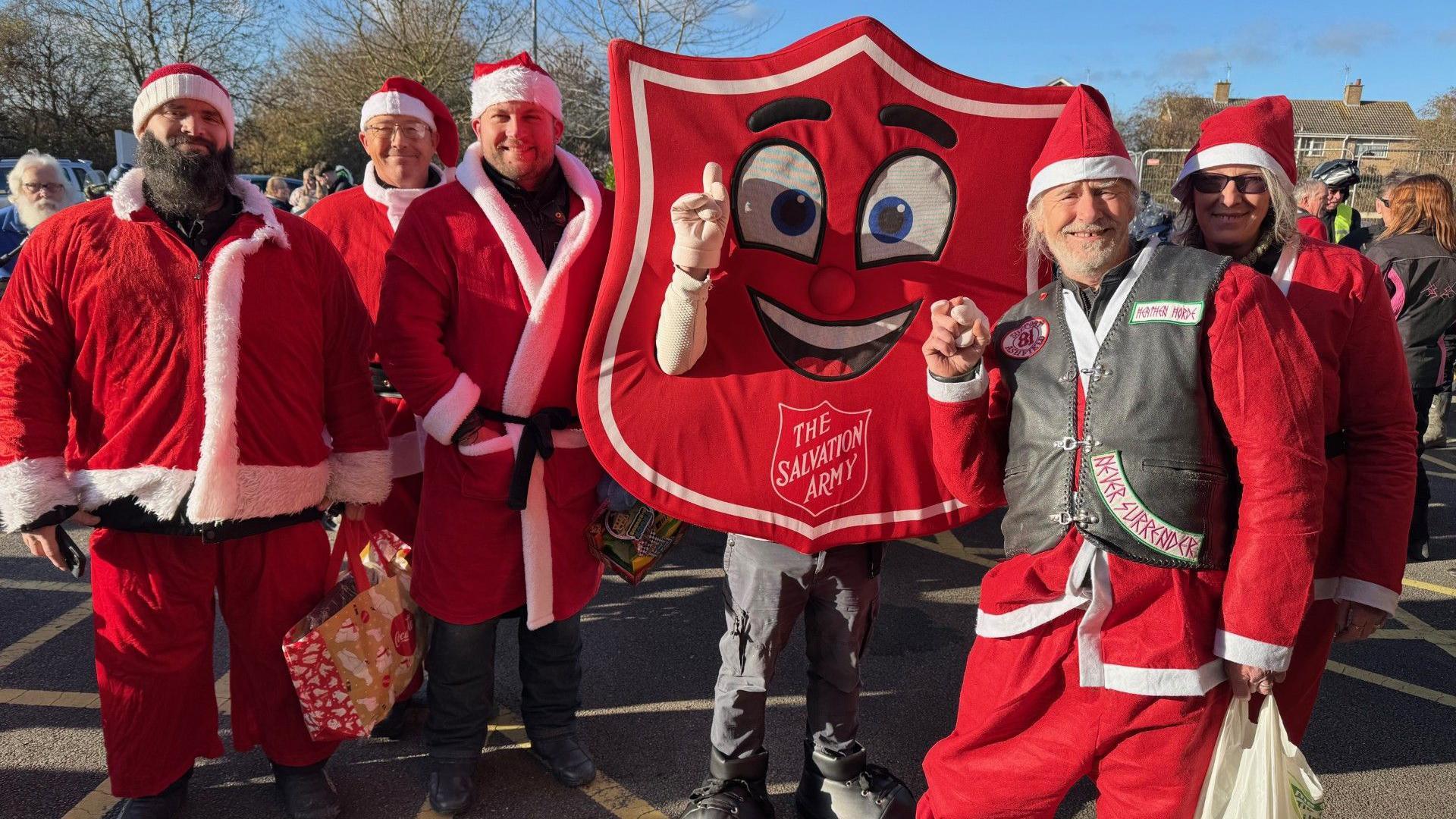 Five bikers are dressed as Father Christmas and stand with a person dressed in a Salvation Army tabbard