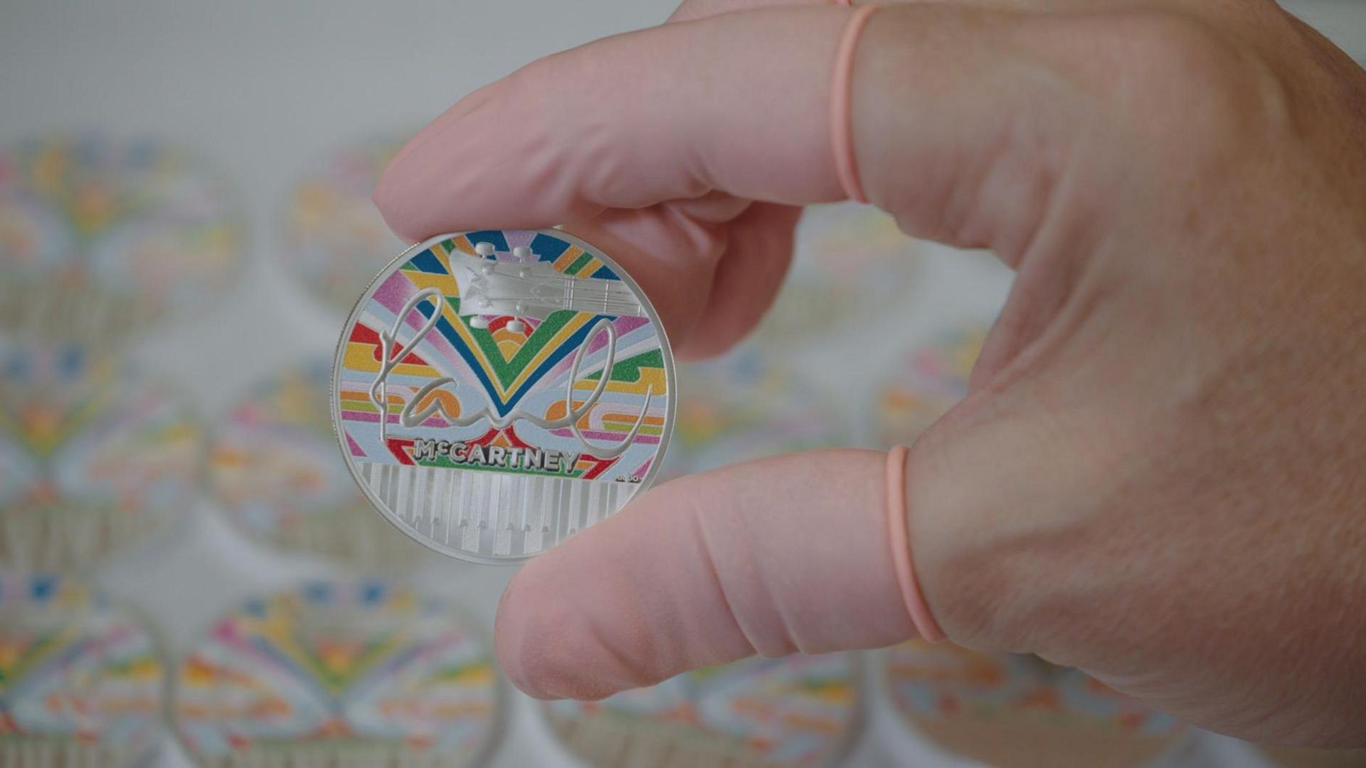 A silver coin with rainbow design being held