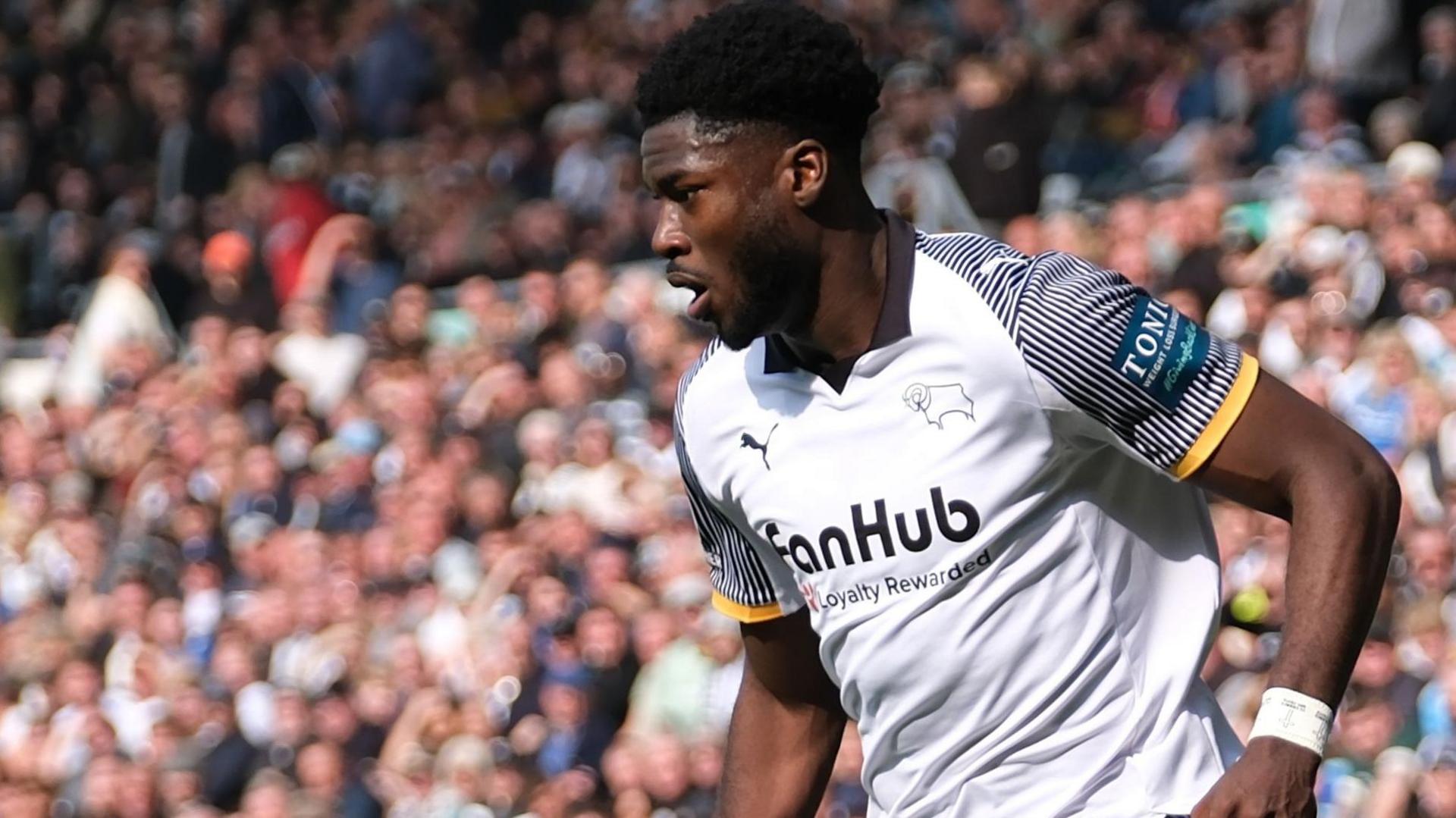 A photo of Patrick Agyemang running with the ball in a black and white Derby home kit in front of the crowd