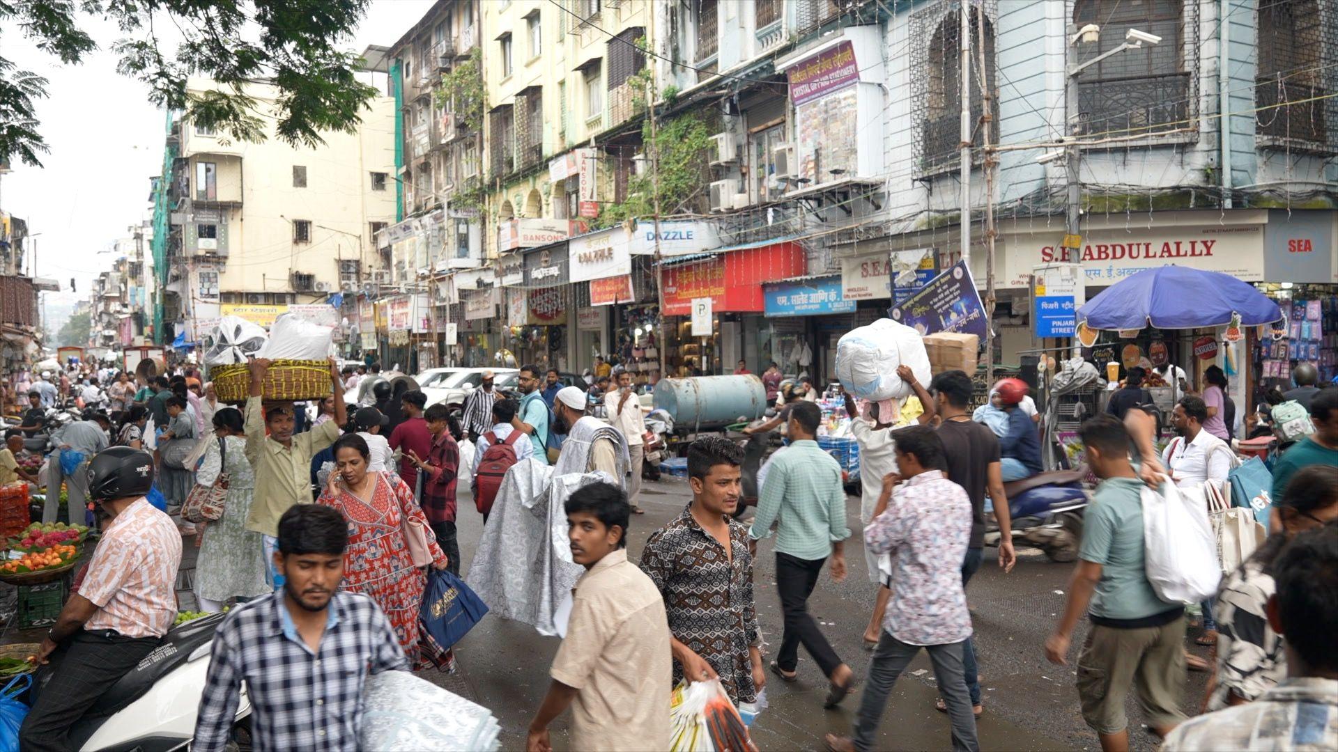 A busy street scene with roadside vendors and cloth merchants carrying their goods in Mumbai's Crawford market area. 