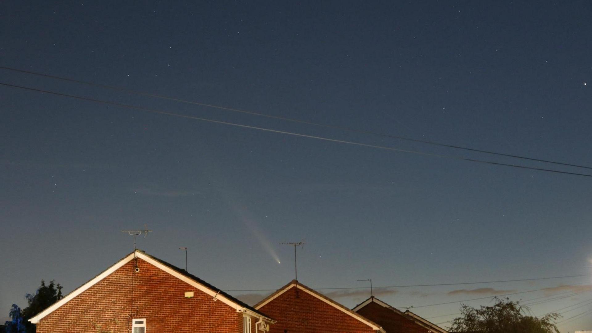 The comet can be seen travelling over rooftops in the early evening sky.  