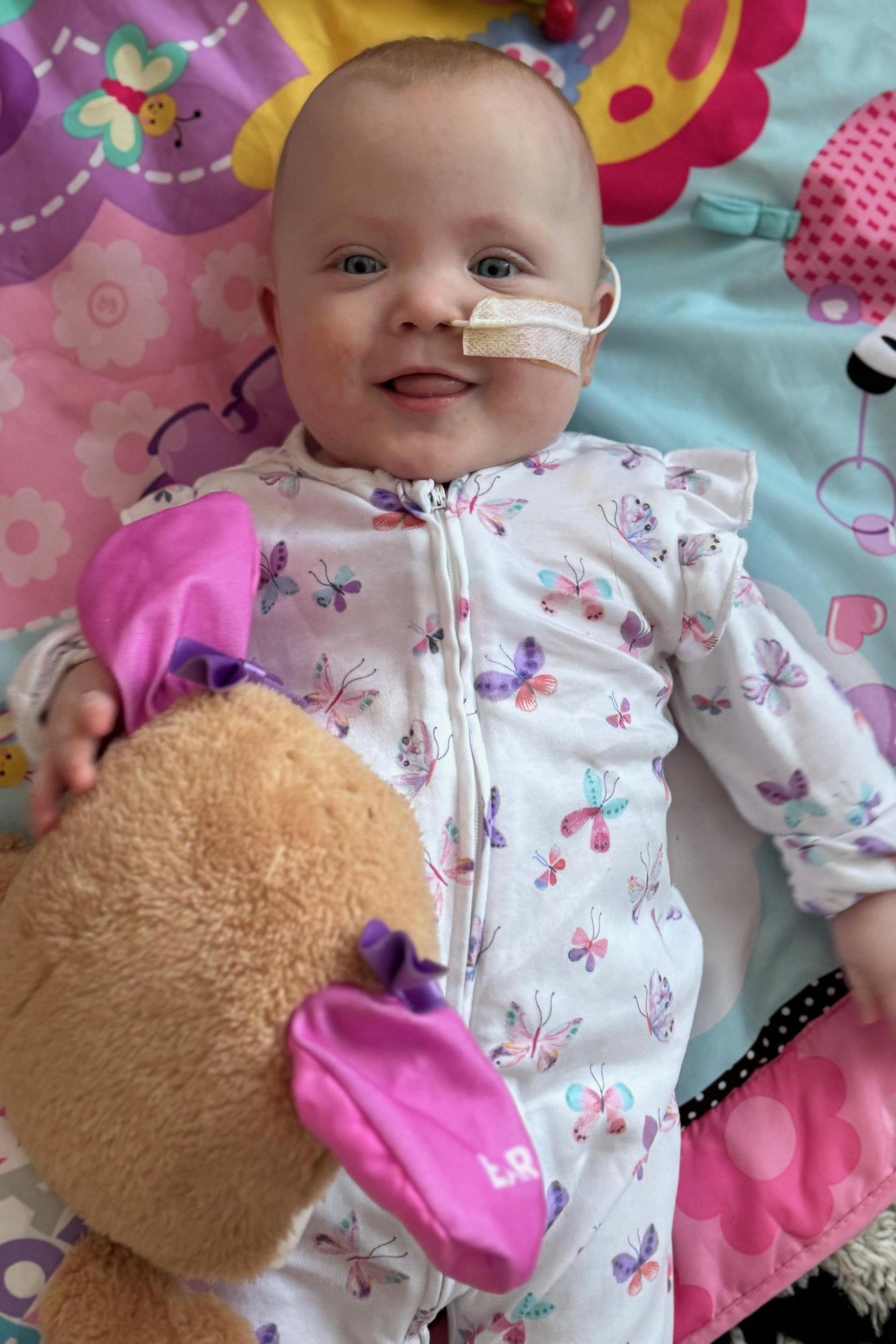 A young baby, smiling, and clutching a stuffed toy.