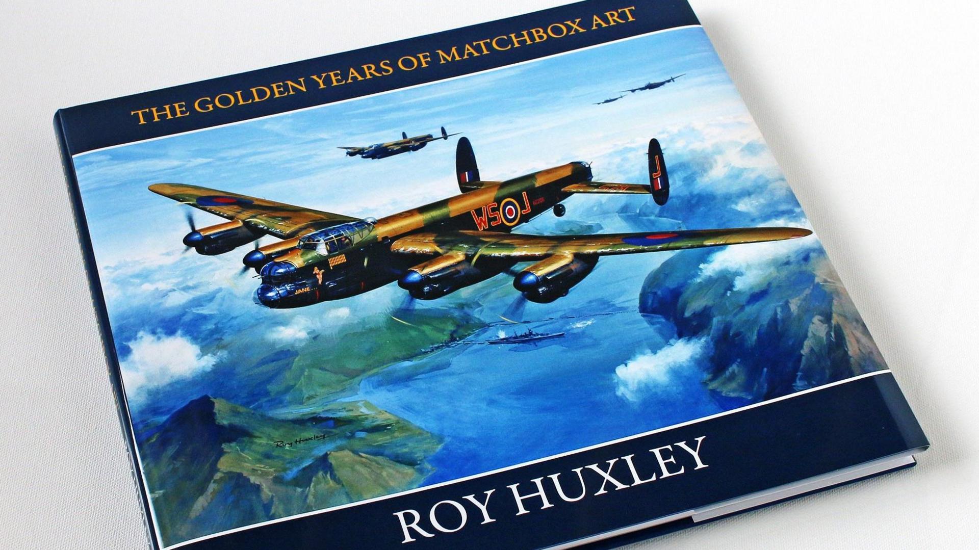 The cover of a hard-backed book. The cover features a painting of four military aircraft flying over blue water, white blobs of cloud, and green hills. A ship is sailing on the water below the planes. Across the top of the cover are the words: "THE GOLDEN YEARS OF MATCHBOX ART", written in yellow on a blue background. Across the bottom are the words: "ROY HUXLEY", written in white on a blue background.