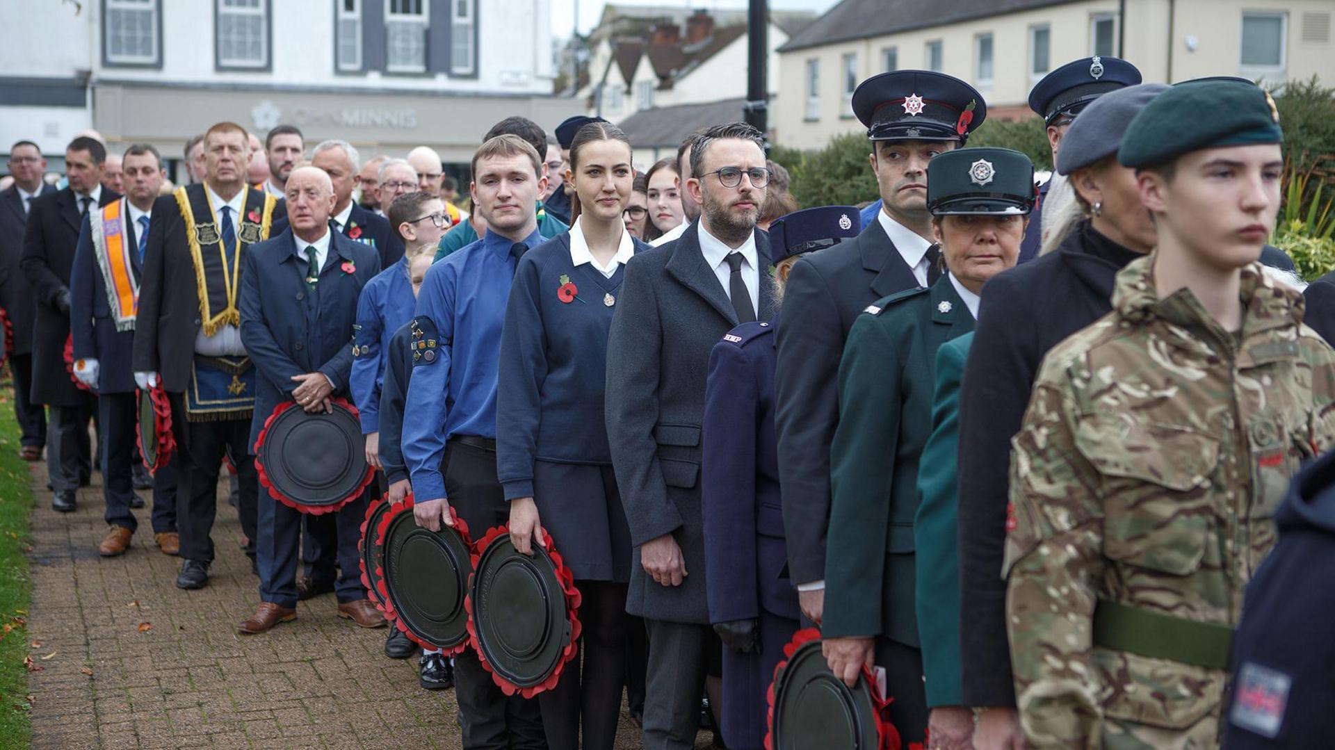 A line of people including people in military dress, police, firefighters, school children, and members of the Orange Order.