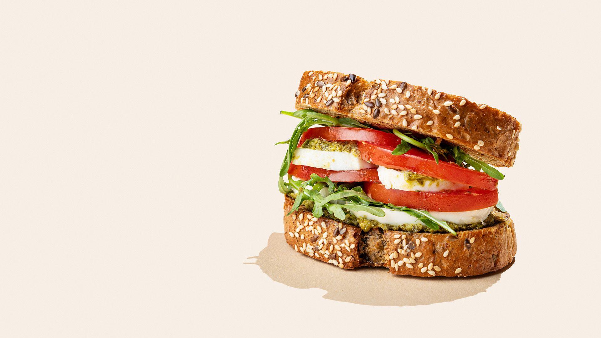 Sandwich of grain bread with tomatoes, mozzarella, arugula and pesto on bright beige background