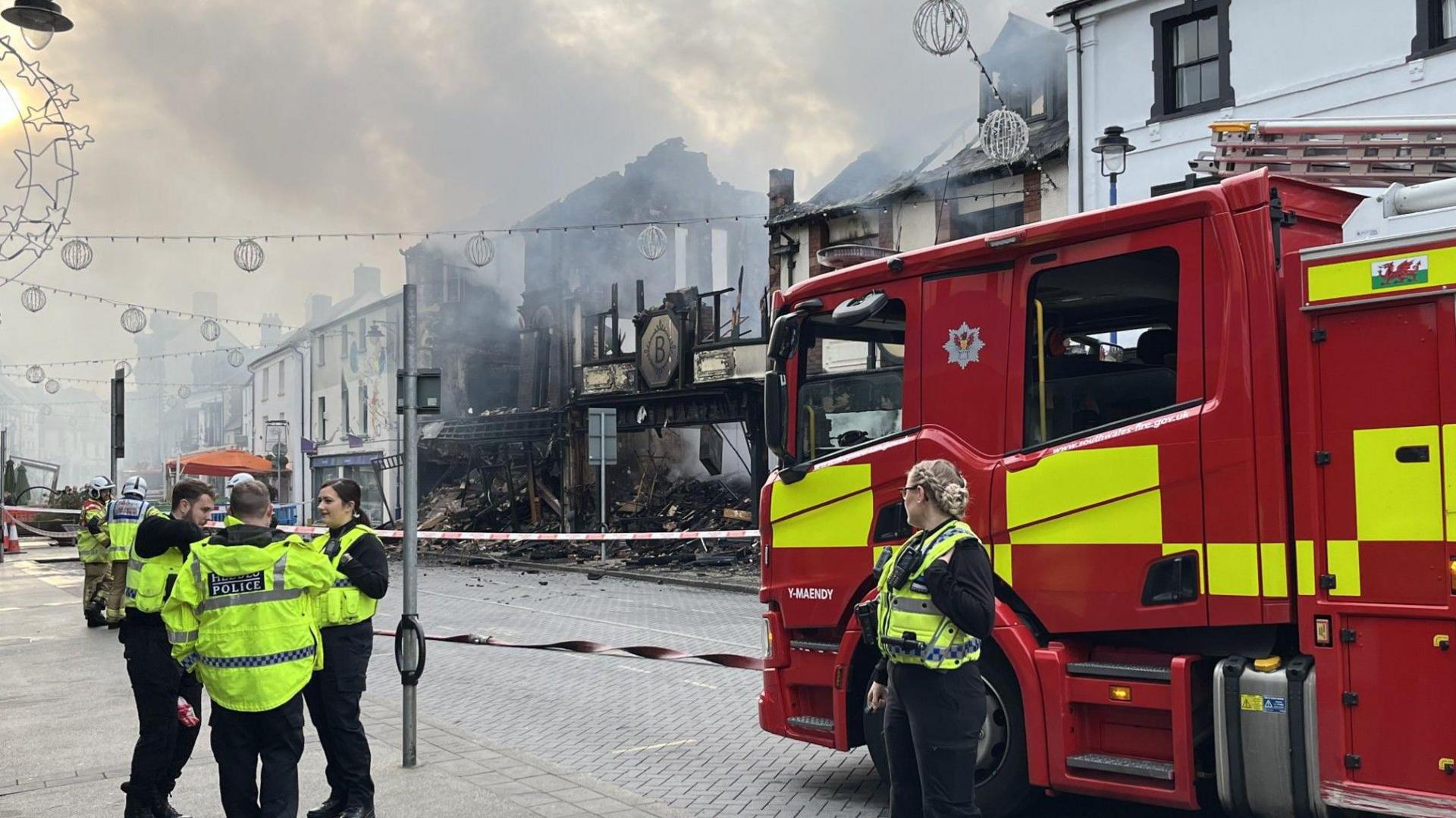 Police and fore workers and a fire truck at the scene with destroyed building in background