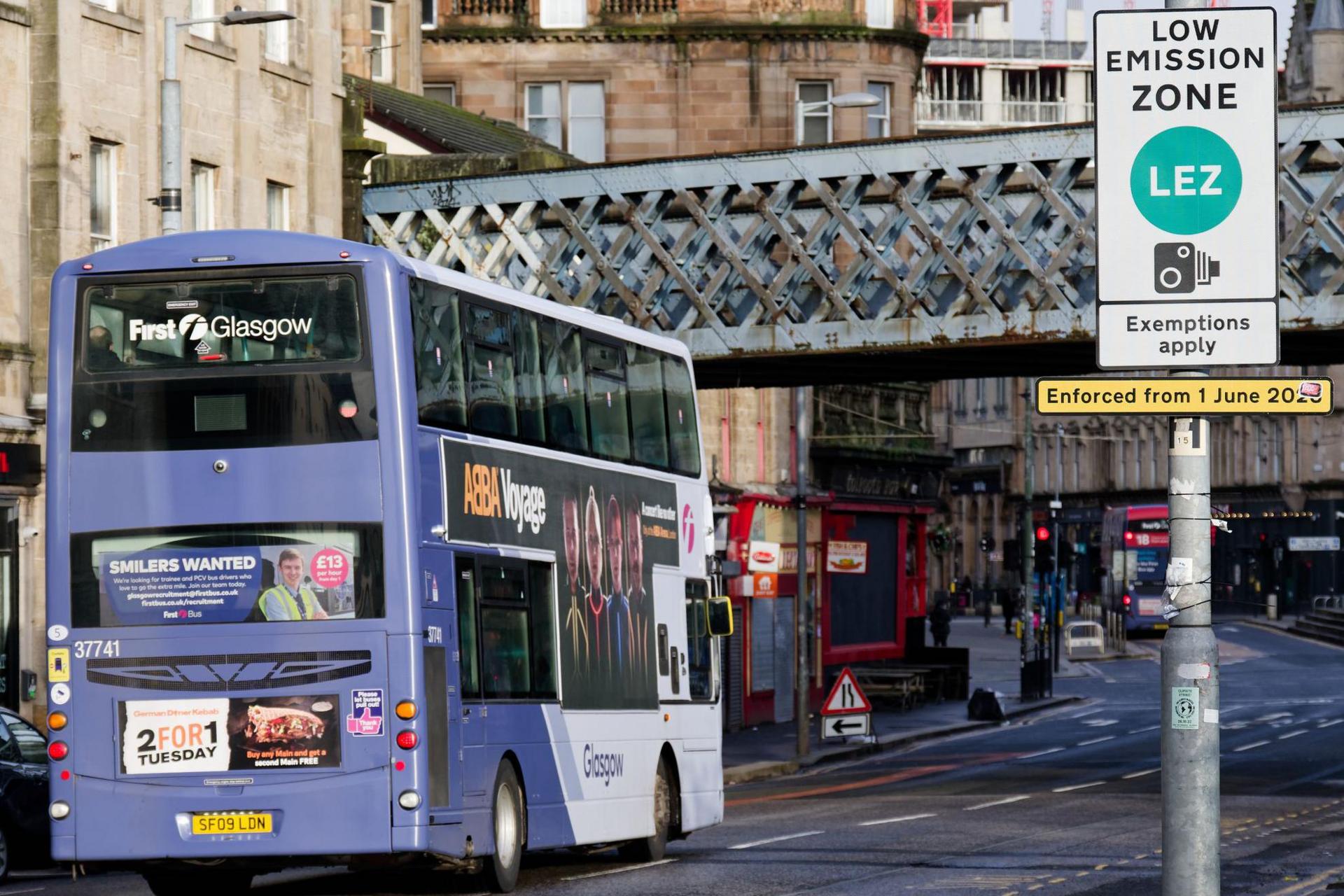 A bus drives past a Glasgow LEZ sign near a bridge