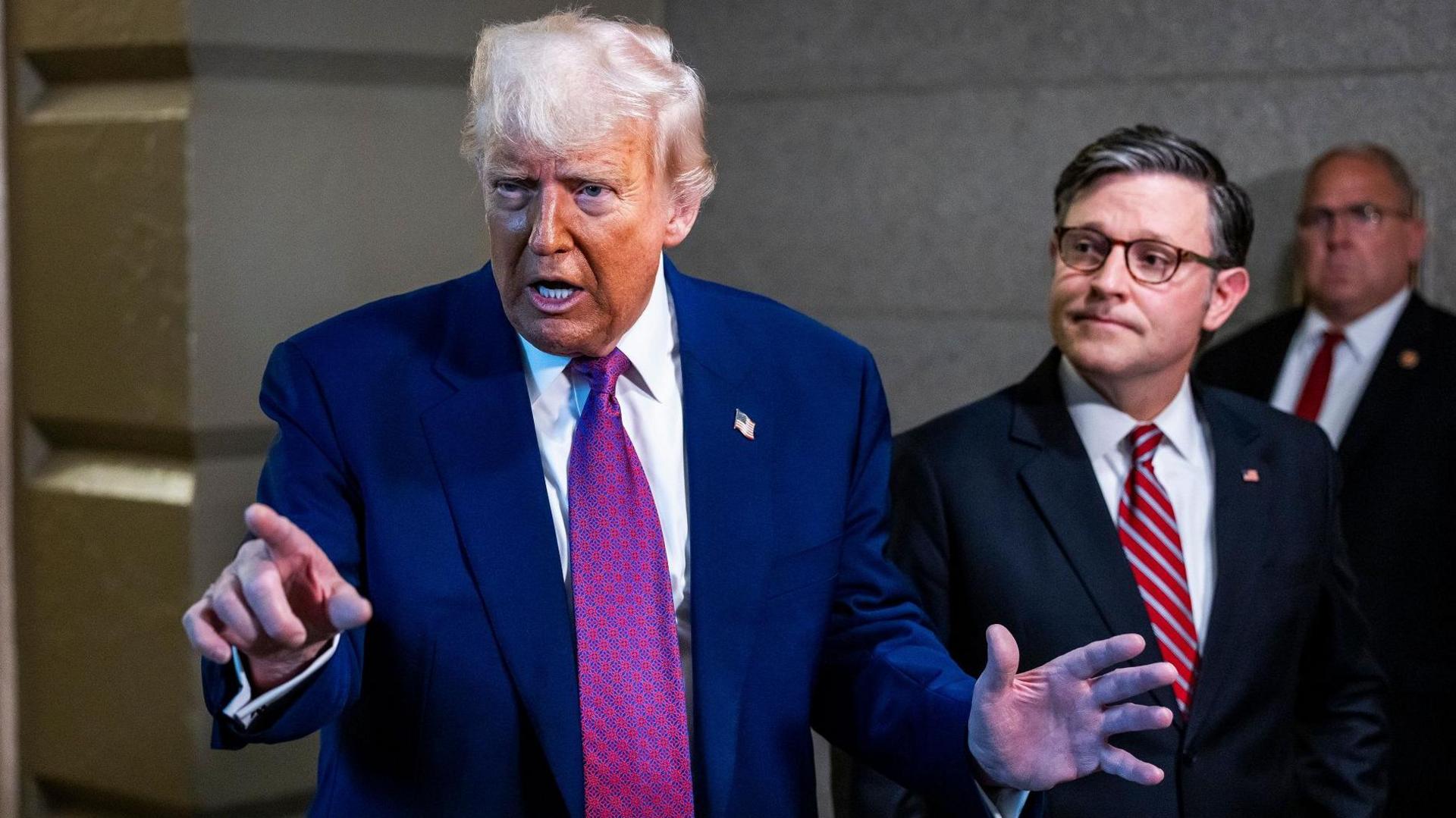 Trump pointing and gesturing as Johnson beside him looks at the president
