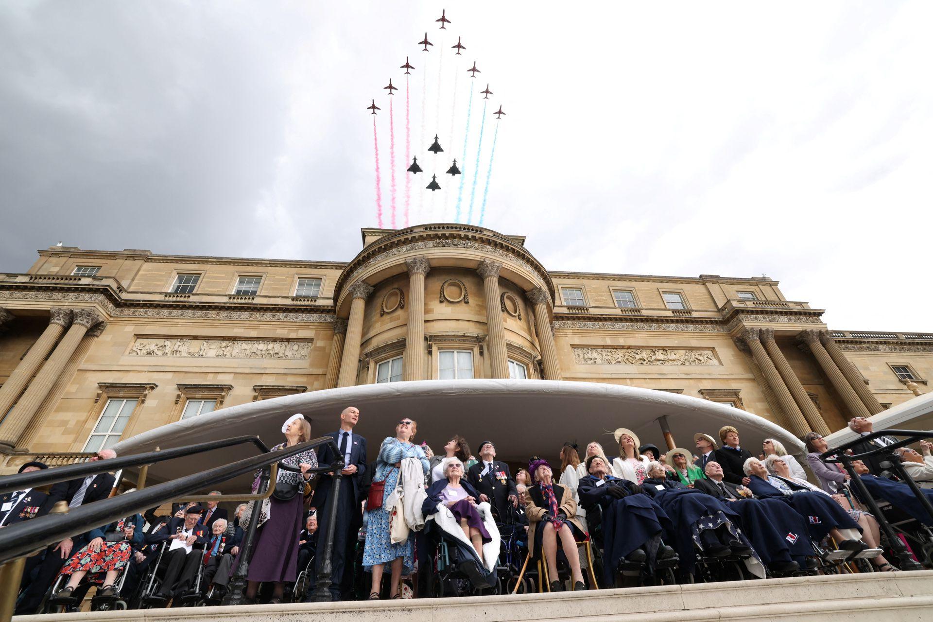 Second World War veterans and other guests look up at the sky as they watch the Red Arrows and other military aircraft fly over Buckingham Palace against a cloudy sky.