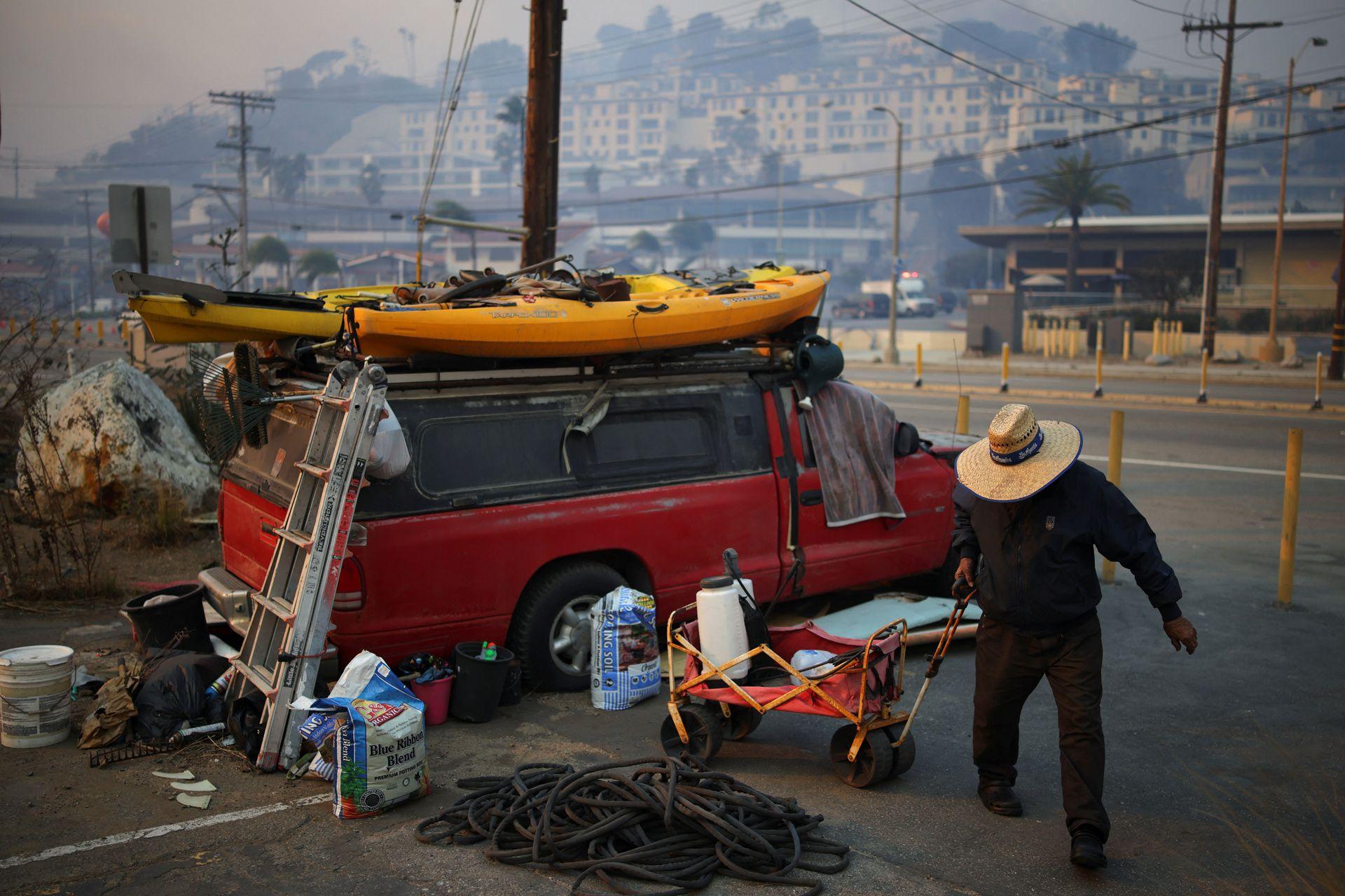 A man in a wide-brimmed hat fetches water while standing next to a red vehicle with a kayak on top of it, along the Pacific Coast Highway on Wednesday.