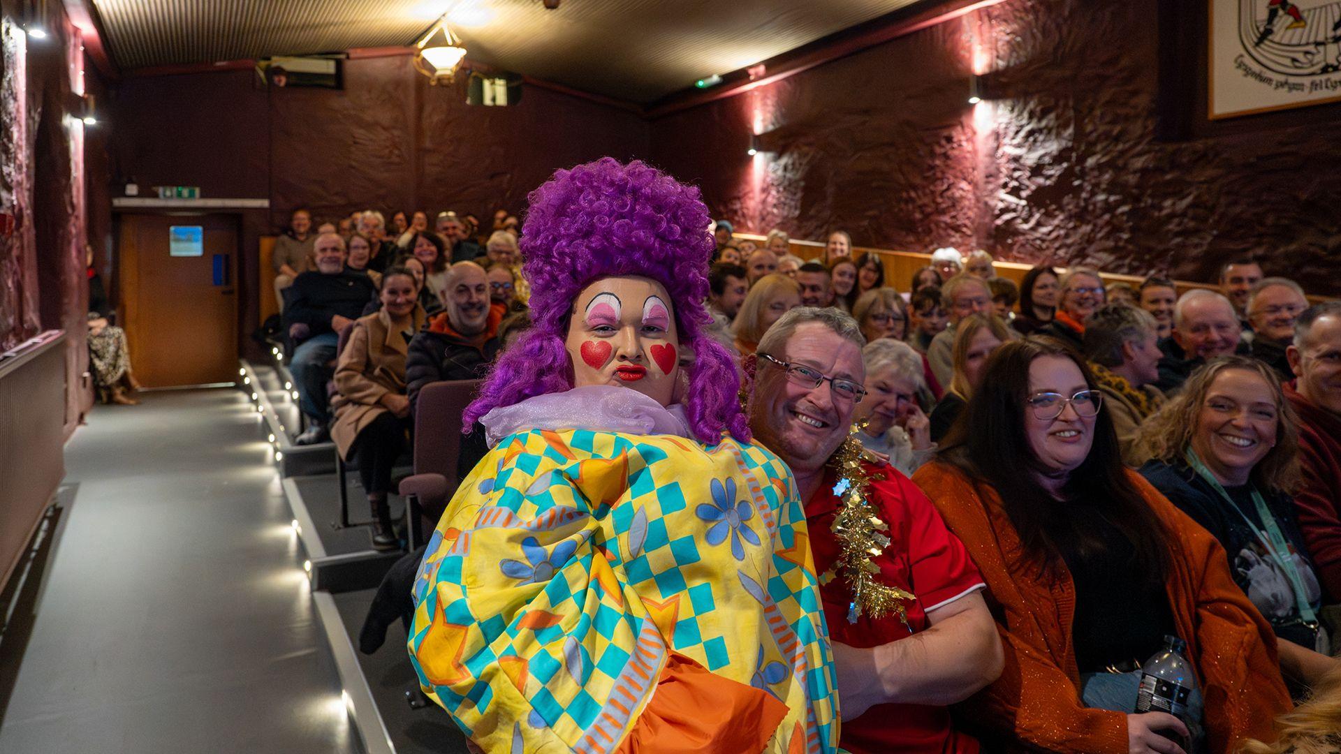 Y Dame yn eistedd ar lin aelod o'r gynulleidfa