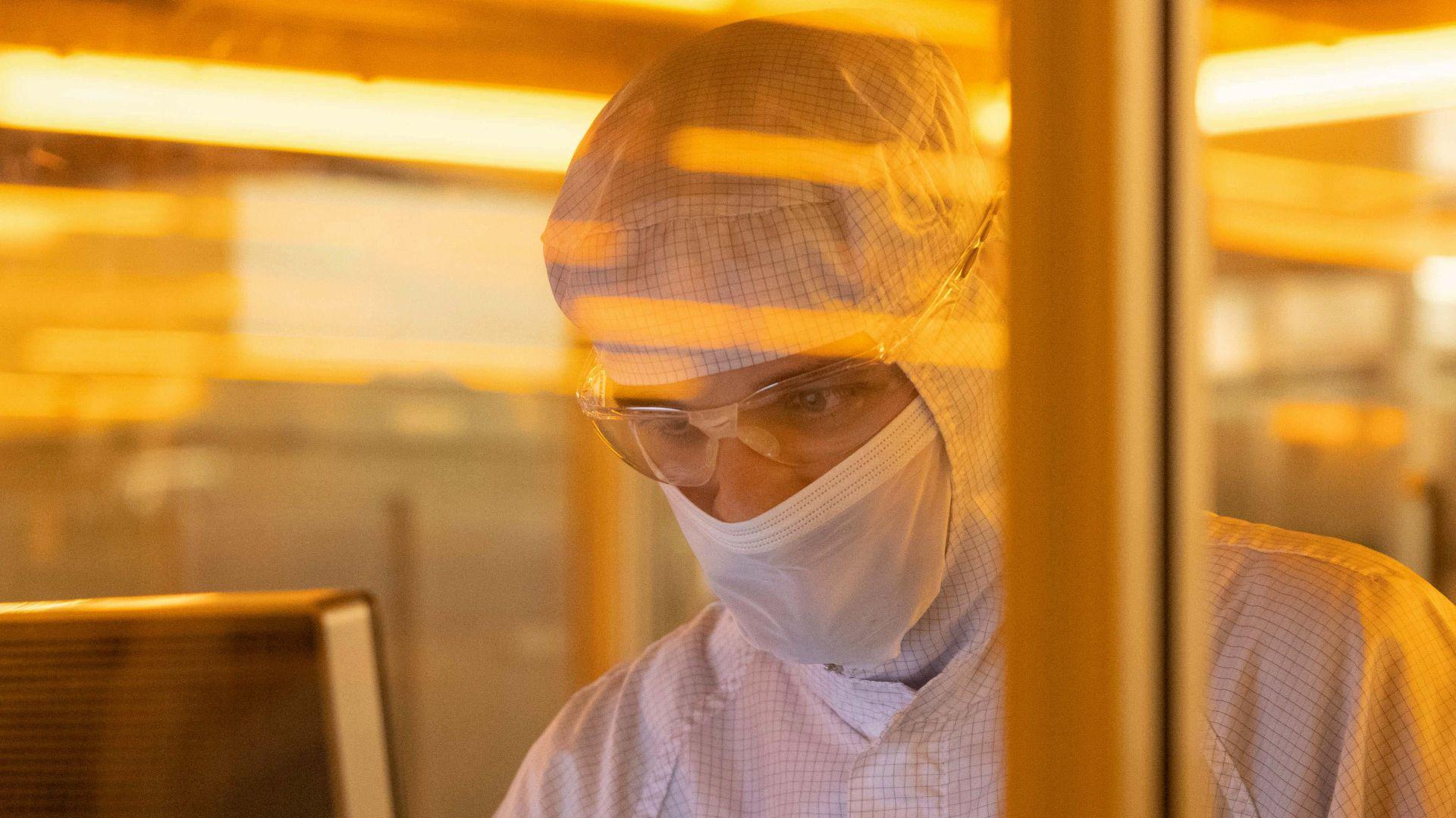 A scientists whose face and head is covered with protective clothing analyses something on a screen.