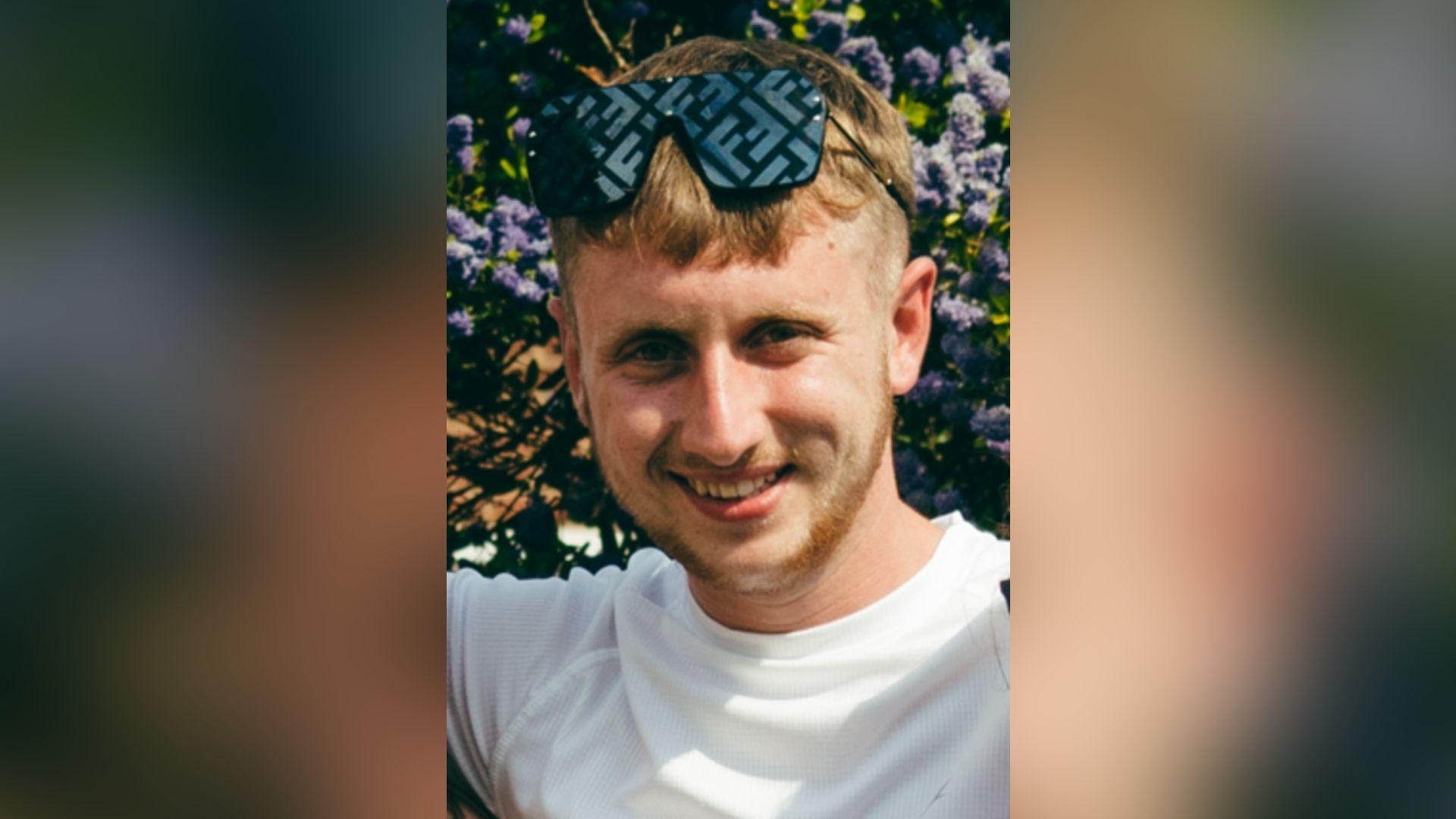 James Roberts, who has short-length blonde hair and facial hair of the same colour. Mr Roberts is wearing a white t-shirt with black sunglasses over his head.