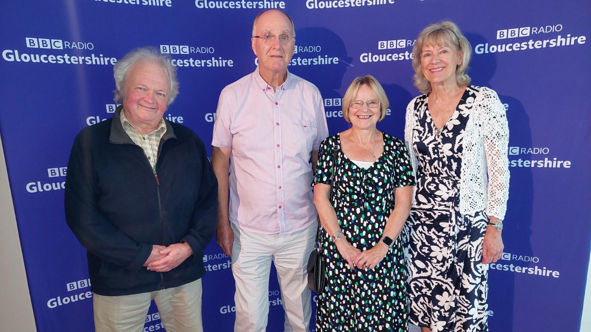 Two older men and two older women stand in front of a purple "BBC Radio Gloucestershire" backdrop, smiling