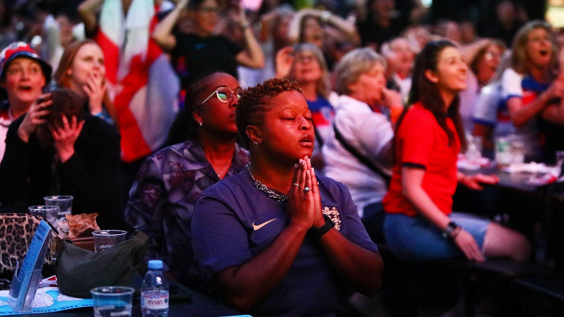 A woman in a blue England T-shirt holds her hands in the prayer position surrounded by fans in Boxpark, Croydon, London, in a particularly tense moment during the semi-final between England and Italy 